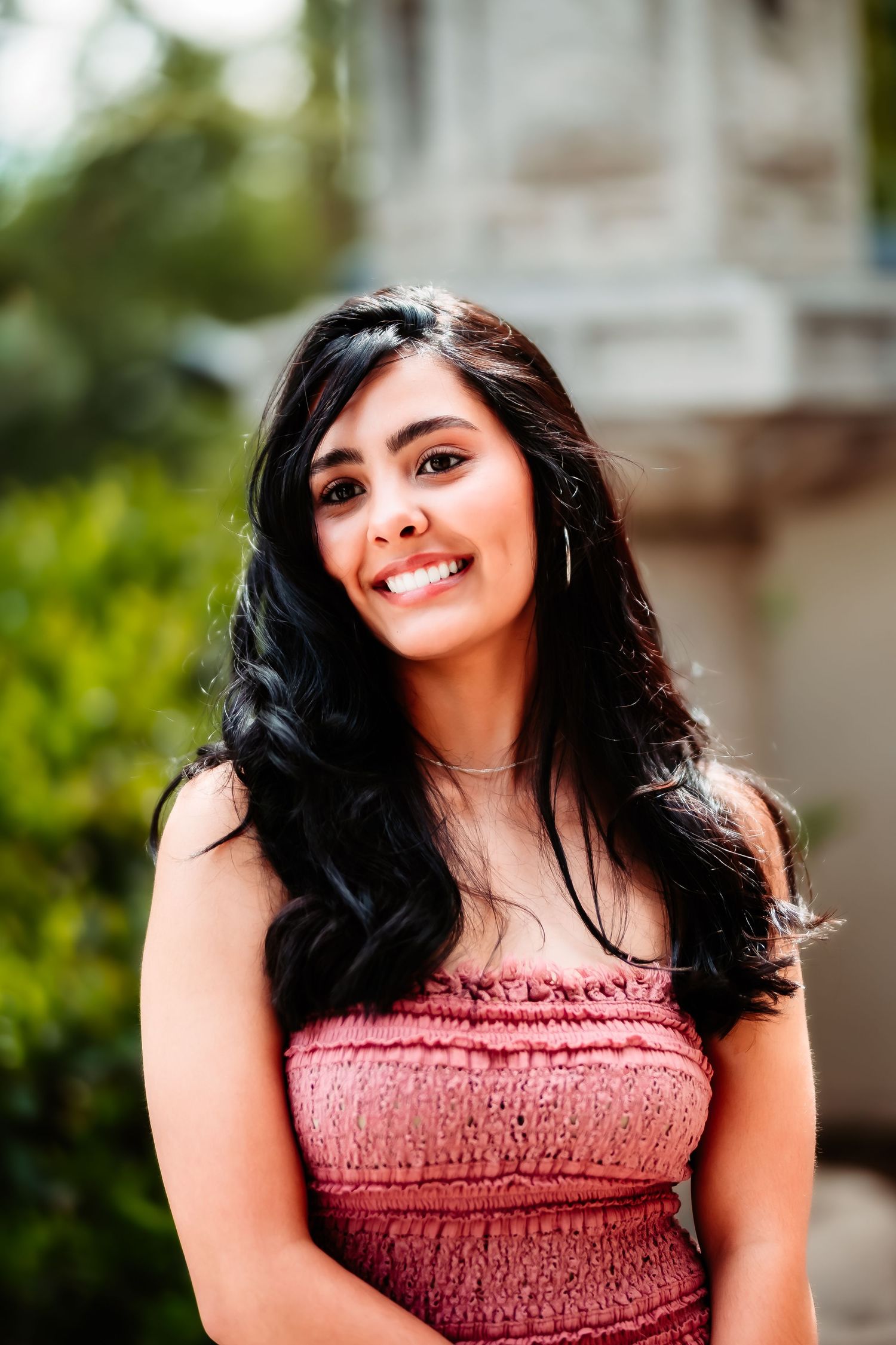 Woman in pink strapless dress smiling outdoors with blurred garden background.