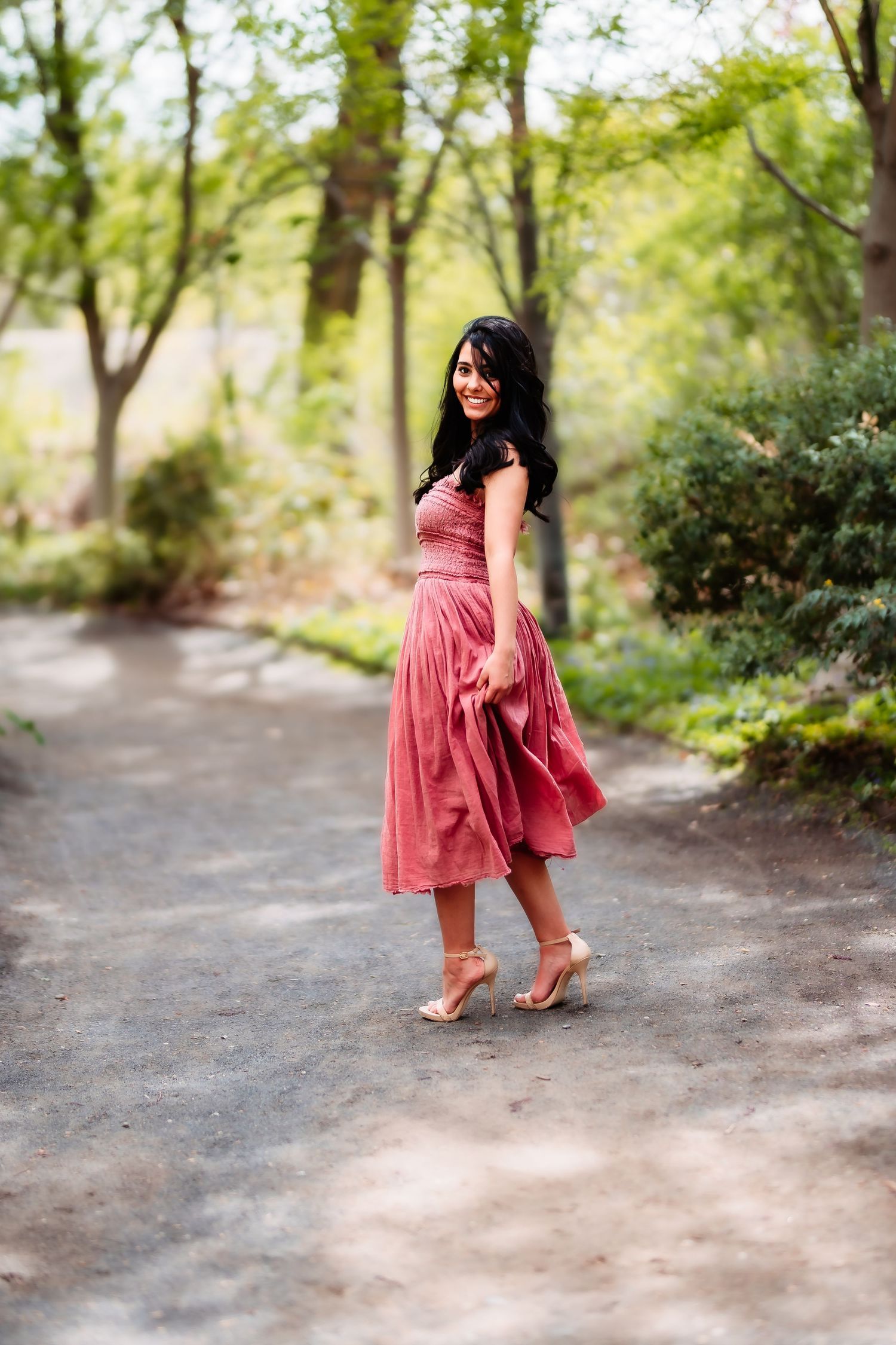 Person in a flowing pink dress standing on a path surrounded by lush greenery.