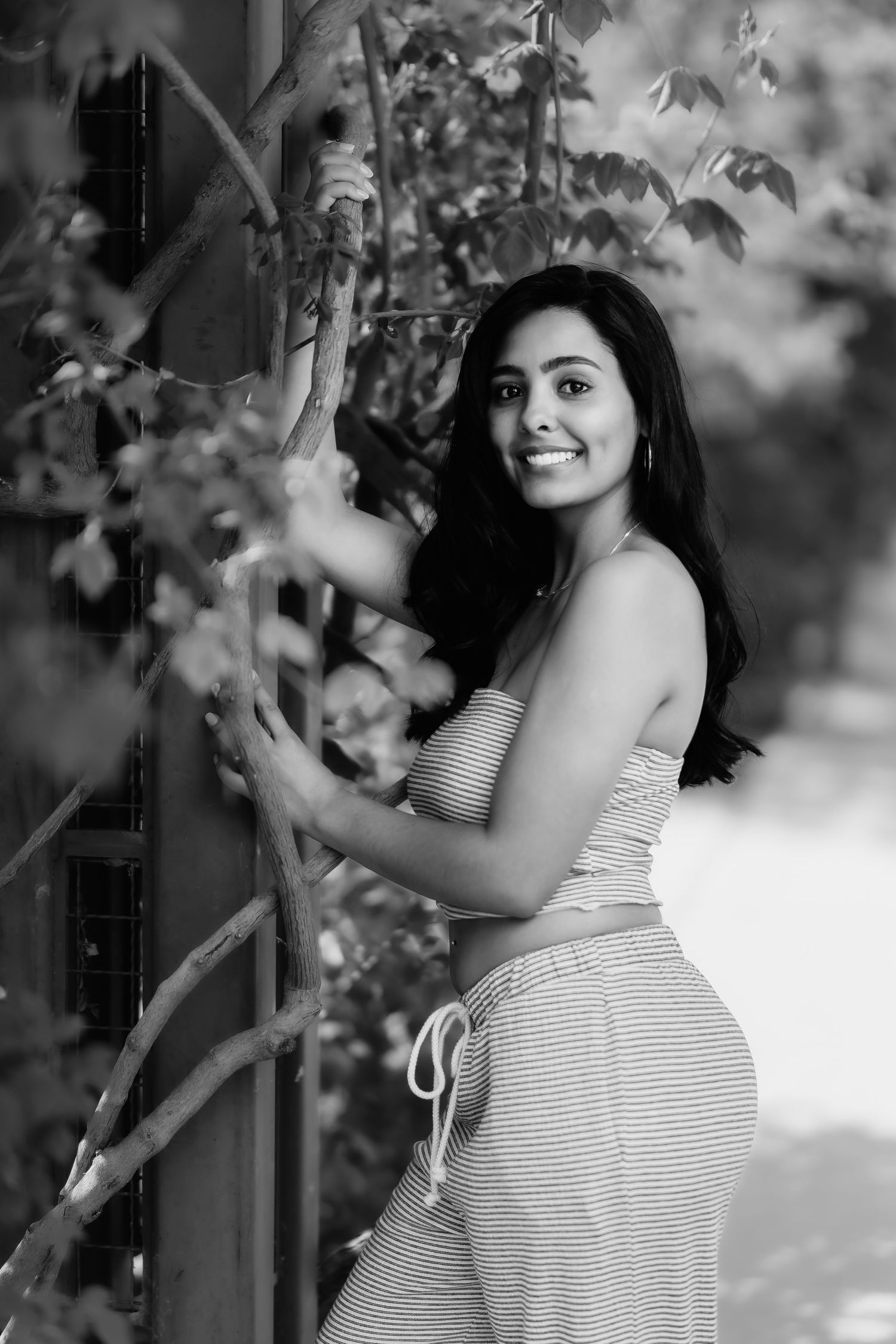 A black and white portrait shows someone in a striped dress posing gracefully next to foliage.