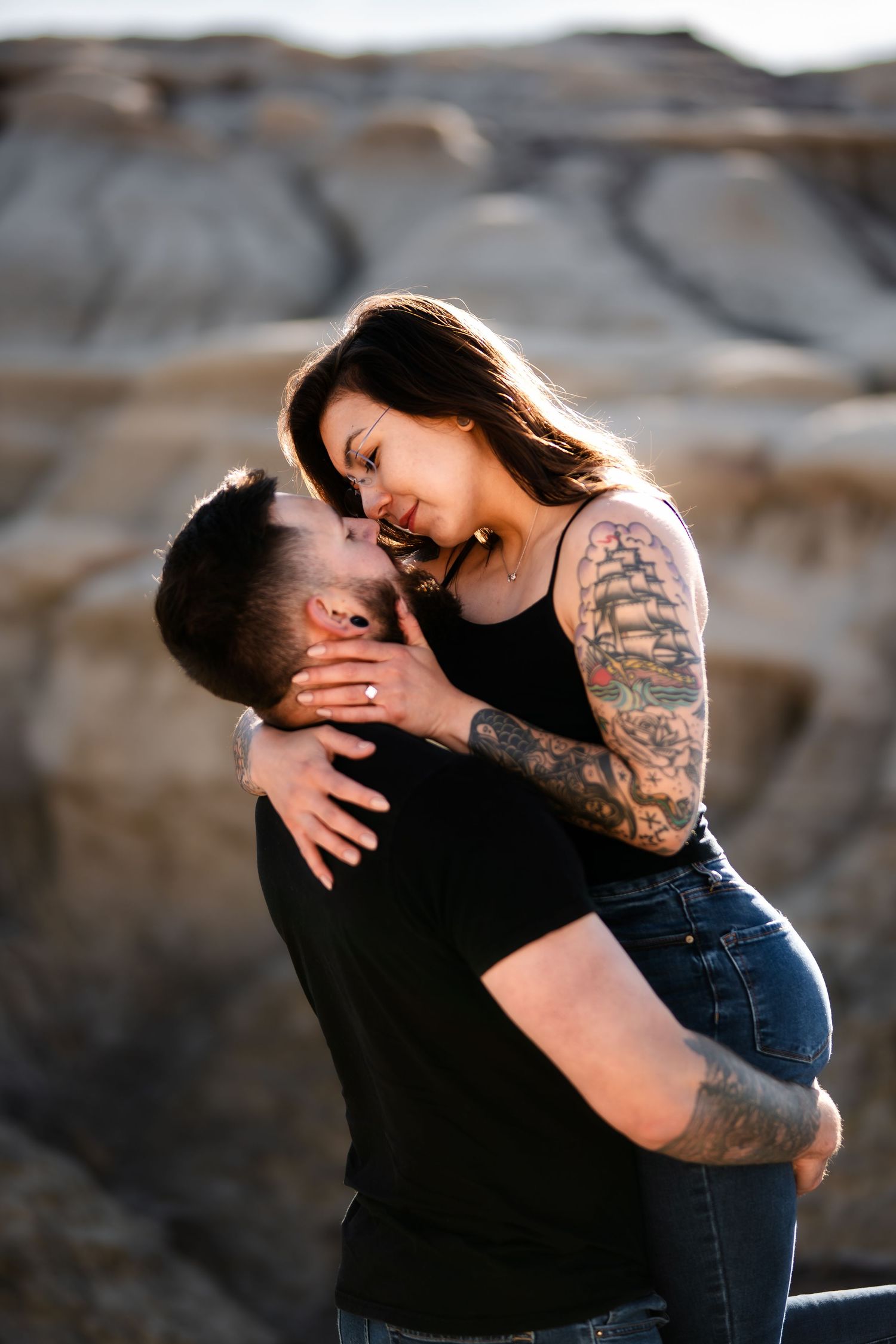 Intimate moment between couple with tattoos against rocky desert backdrop.