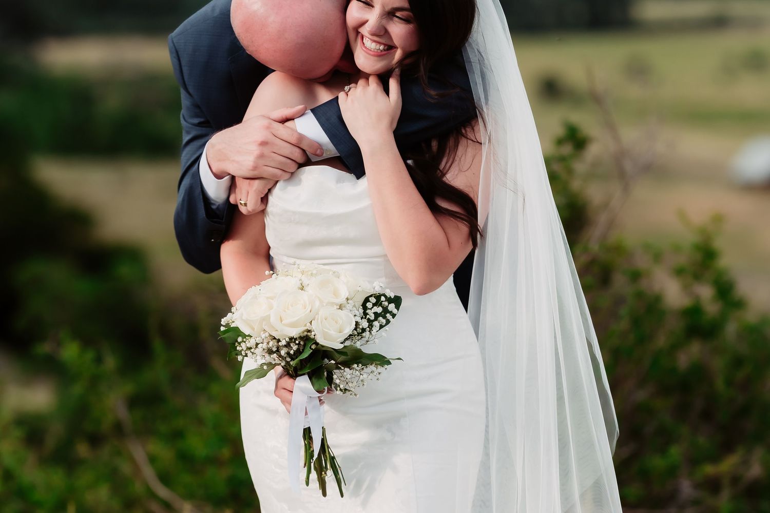 A joyful wedding moment captured outdoors with scenic rolling hills in the background.