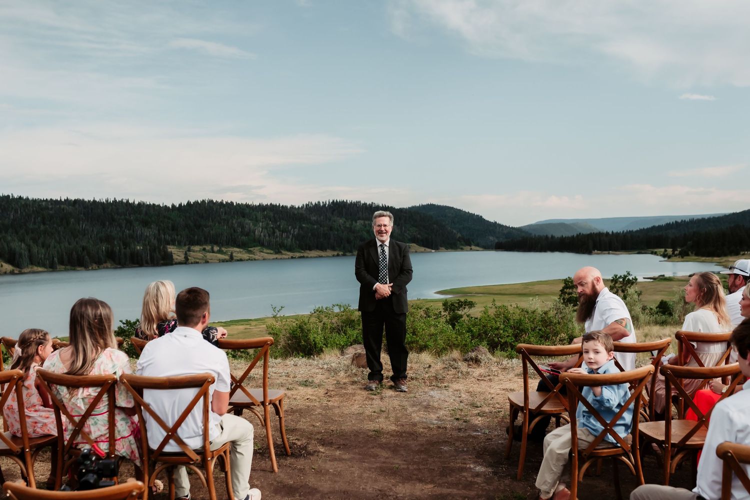 An outdoor wedding ceremony overlooking a scenic mountain lake with rustic wooden chairs.