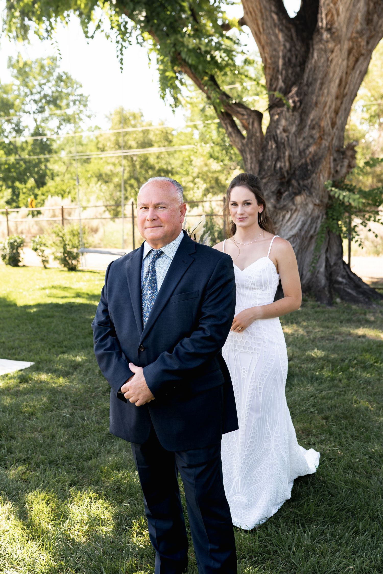 A wedding first look photo with a bride and her escort standing beneath a majestic tree.