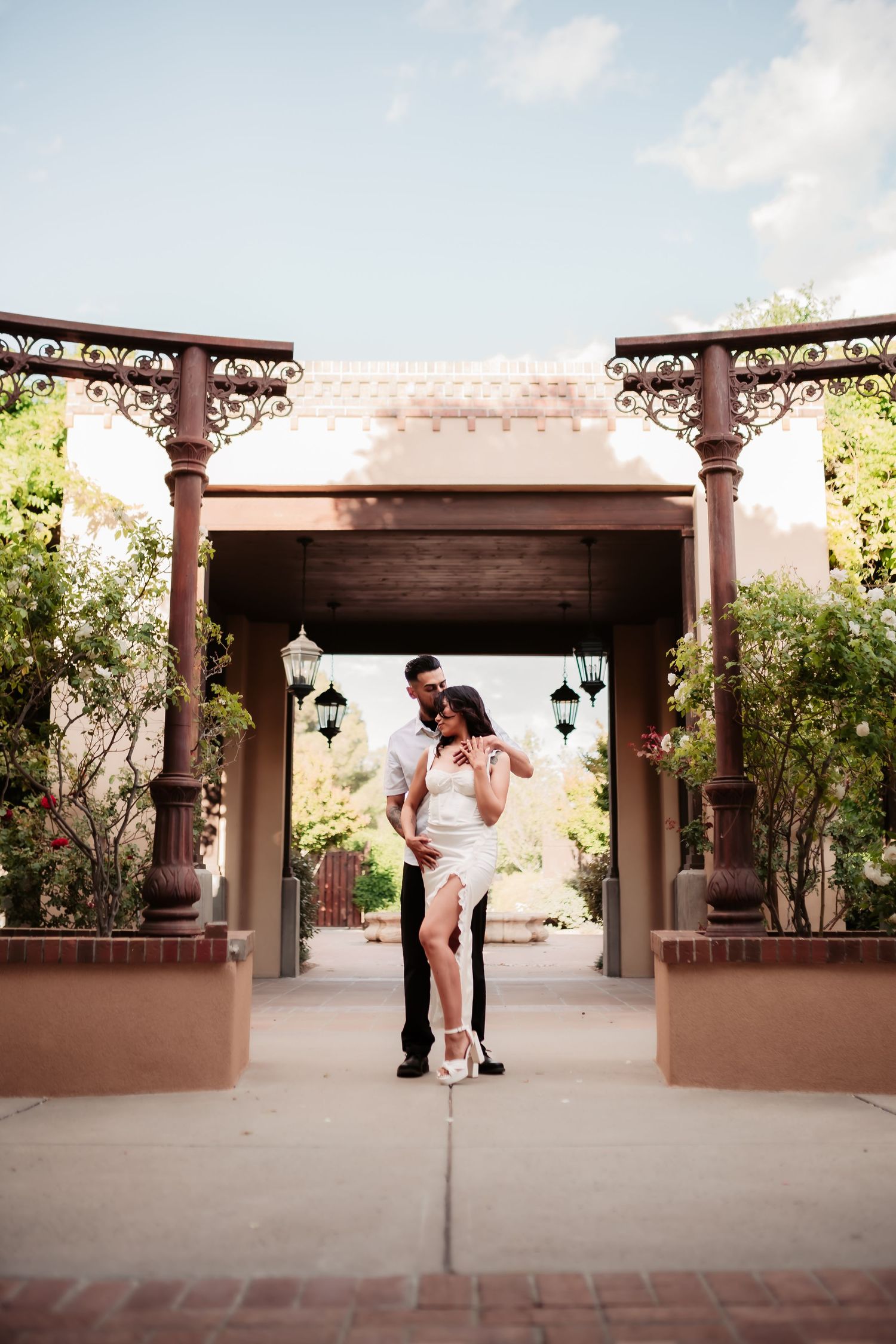 A romantic couple poses under an ornate covered walkway with decorative pillars.