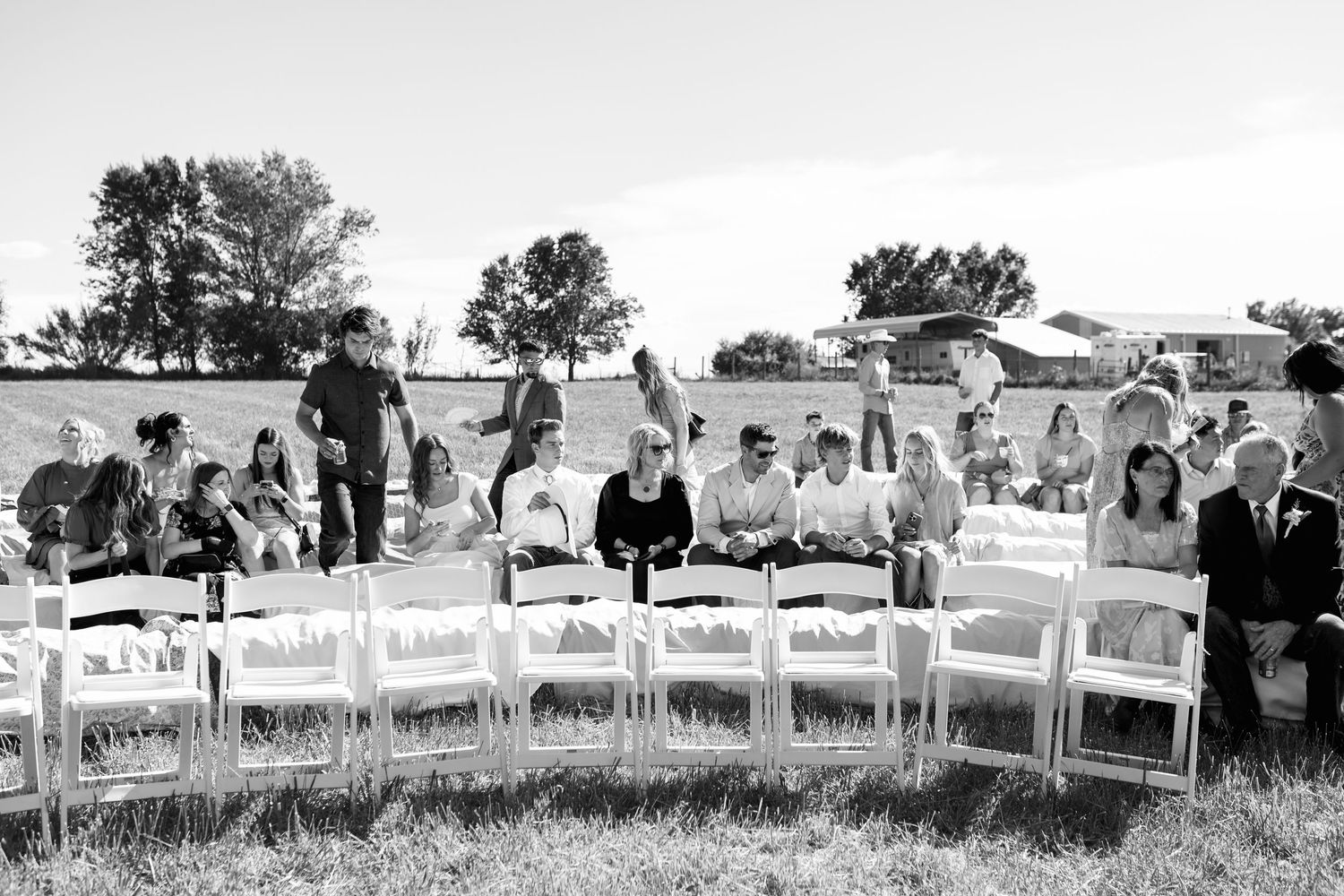 Black and white photo of wedding ceremony setup with white chairs and guests arriving.