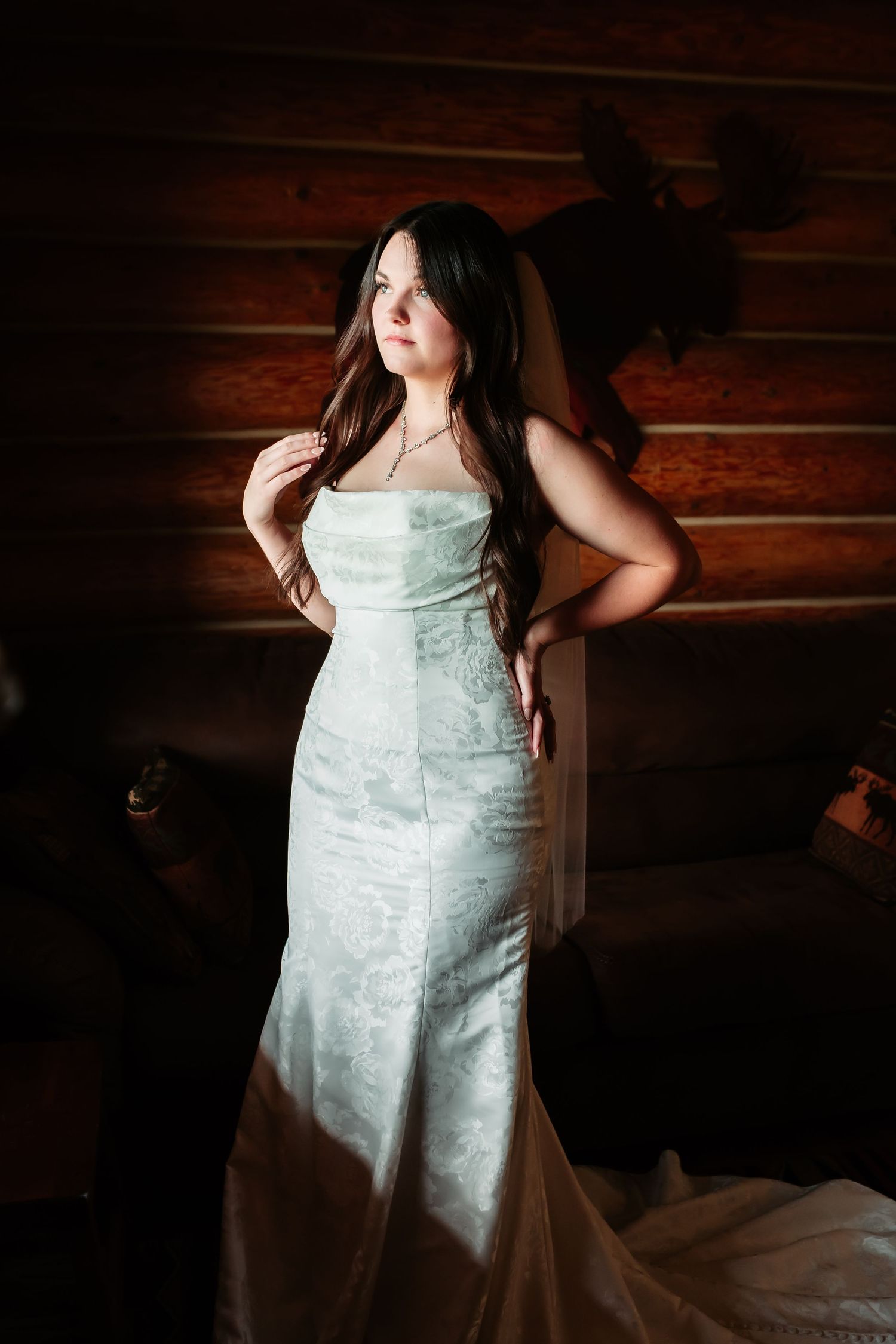 A woman in a fitted white wedding dress poses dramatically against a rustic wooden wall background.