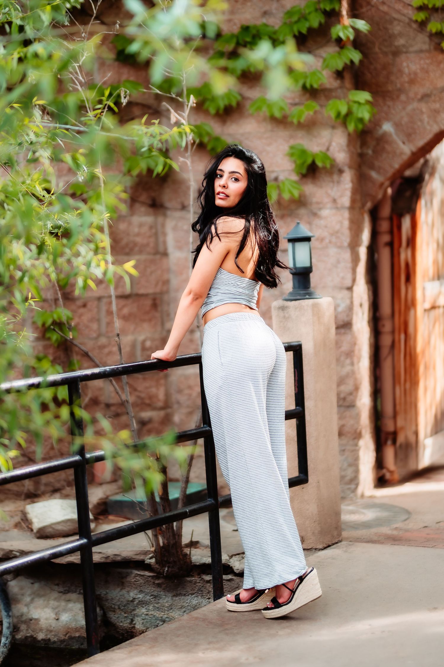 Model in casual athleisure wear poses against rustic wall with climbing vines and lantern.
