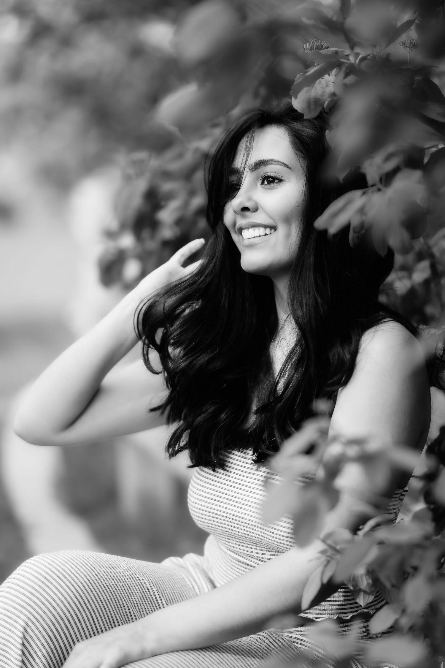 A black and white portrait showing someone in a striped dress posed among leafy branches.