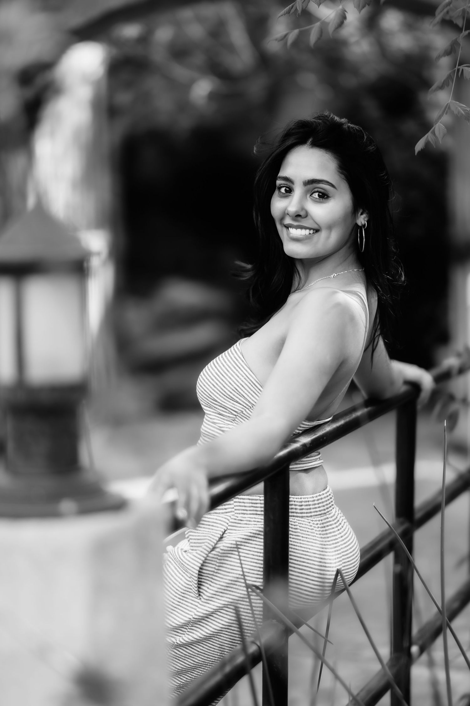 Black and white portrait of woman in striped dress leaning against railing outdoors.