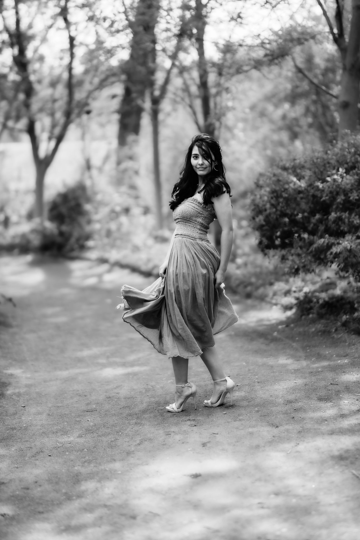 Black and white image of someone twirling in a midi dress on a forest path.
