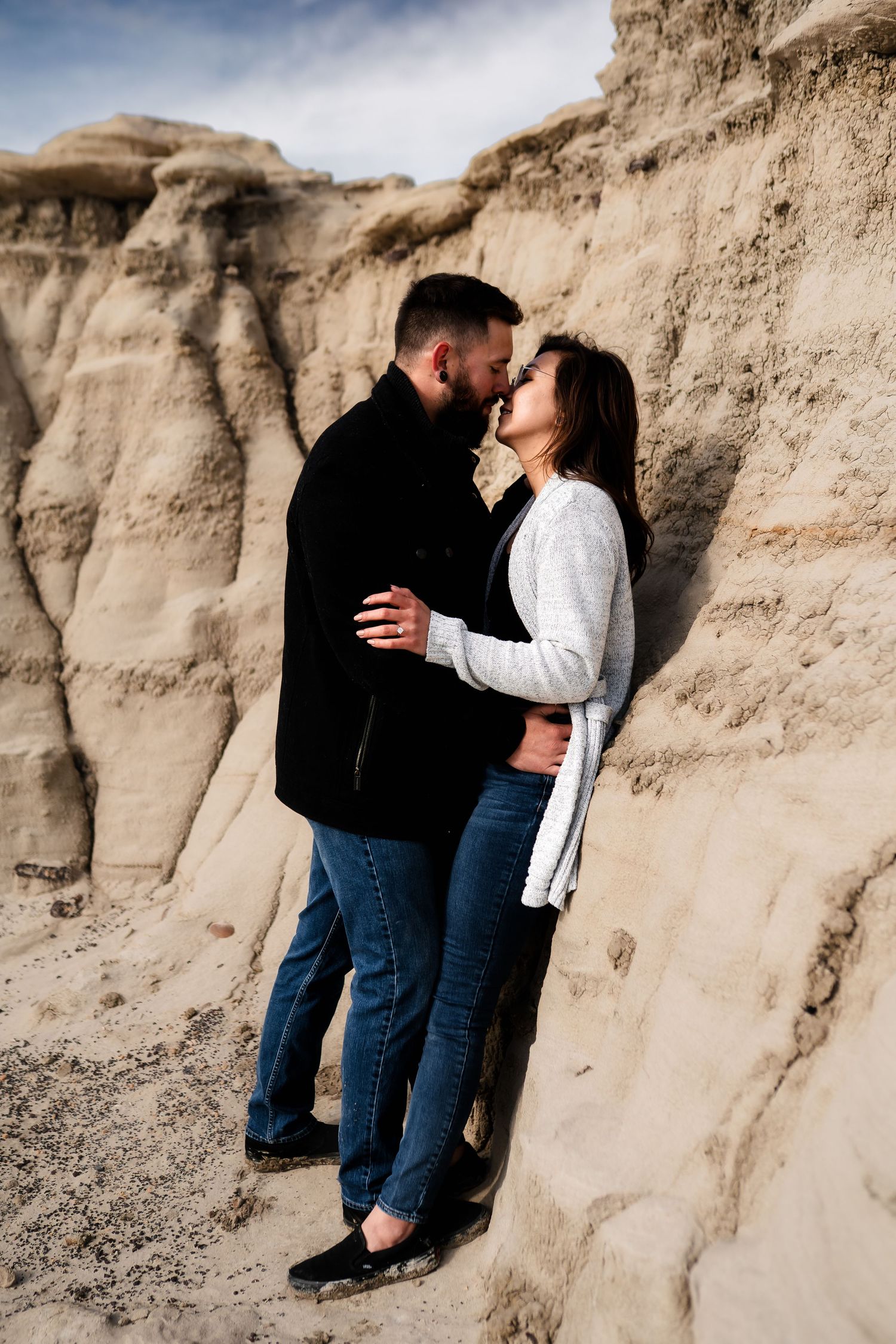 A romantic couple embraces against weathered rock formations wearing casual attire.