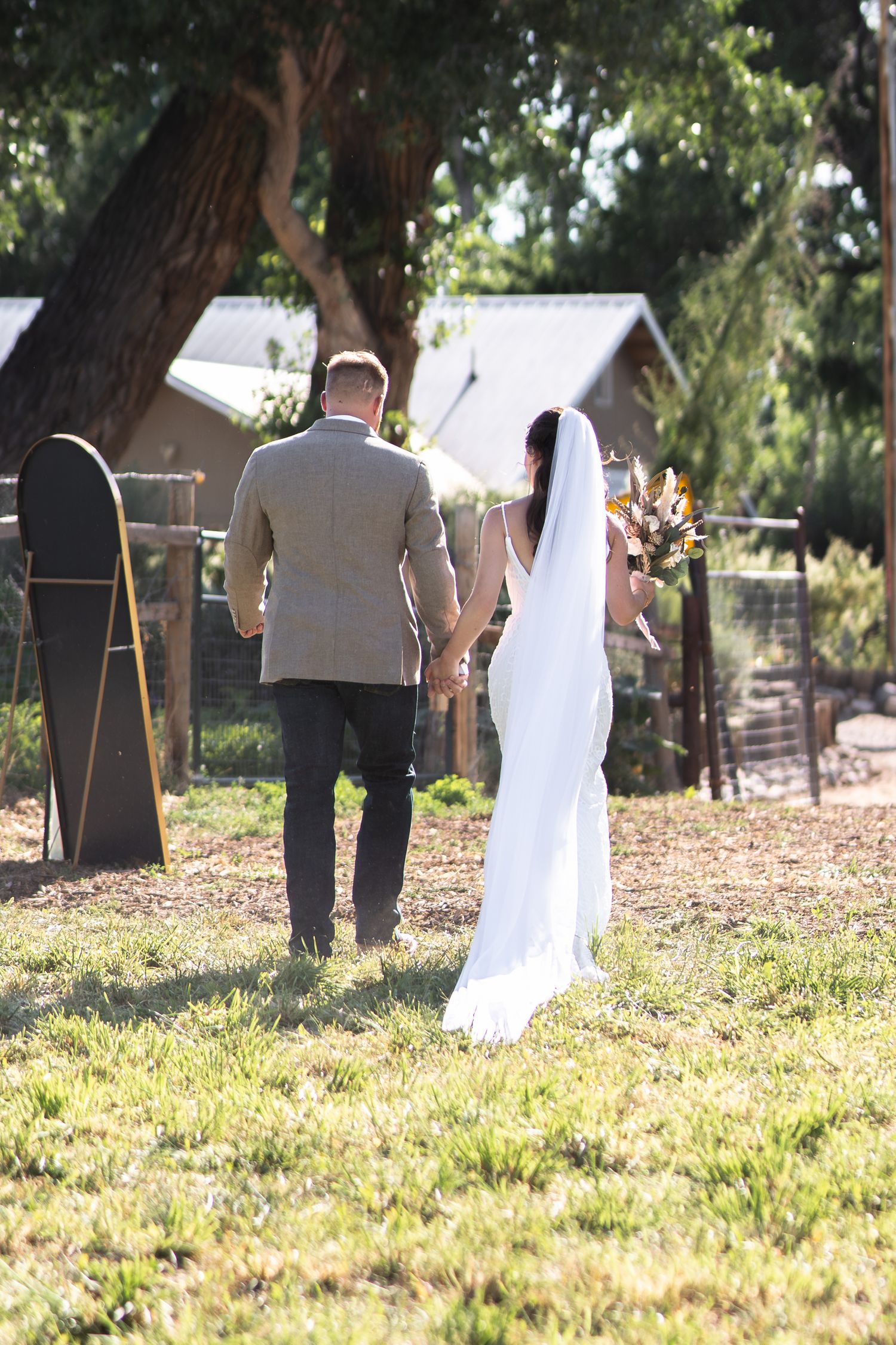A couple standing in a sunny garden during their outdoor wedding ceremony with trees in the background.