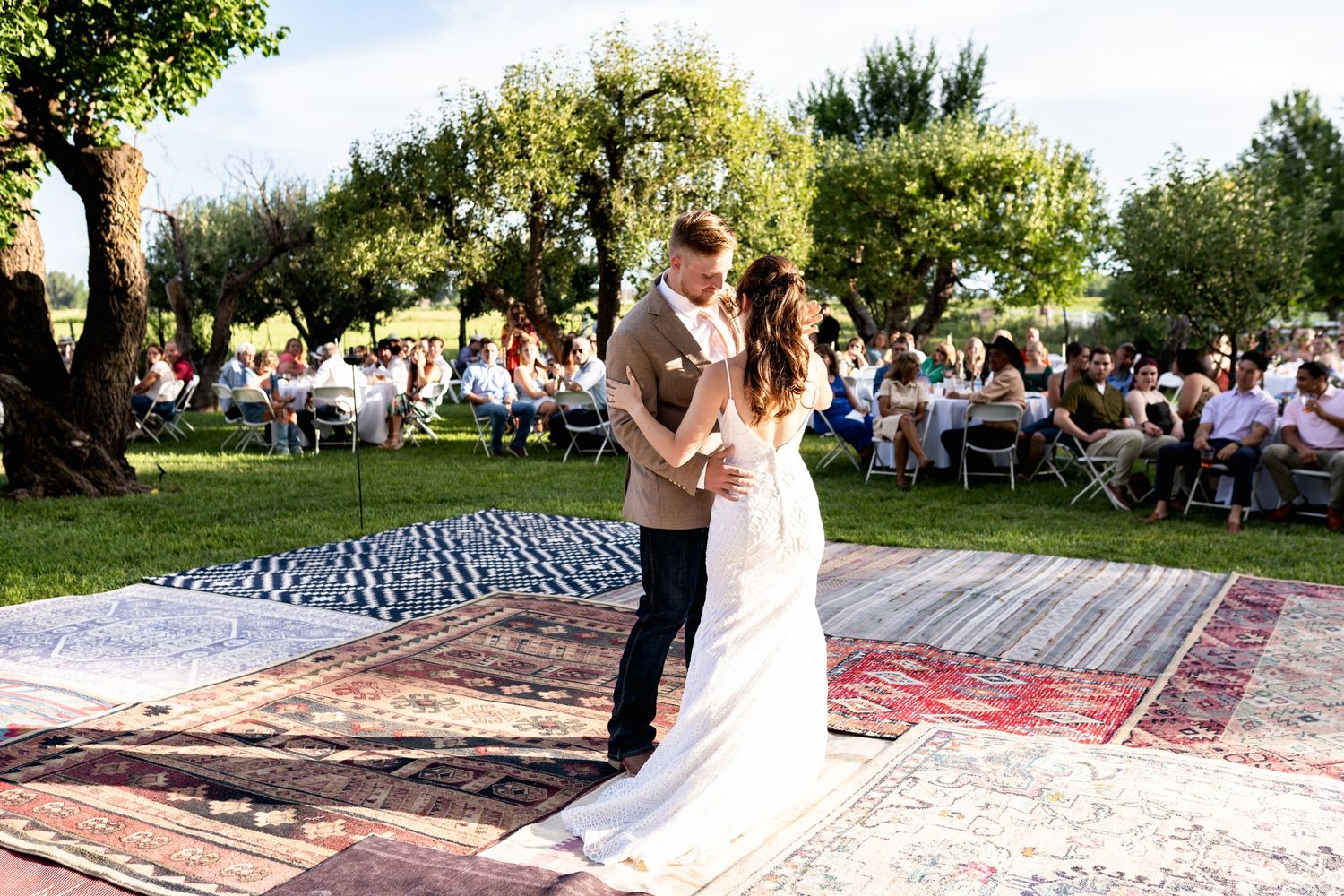 Couple shares first dance on layered vintage rugs with outdoor reception setting.