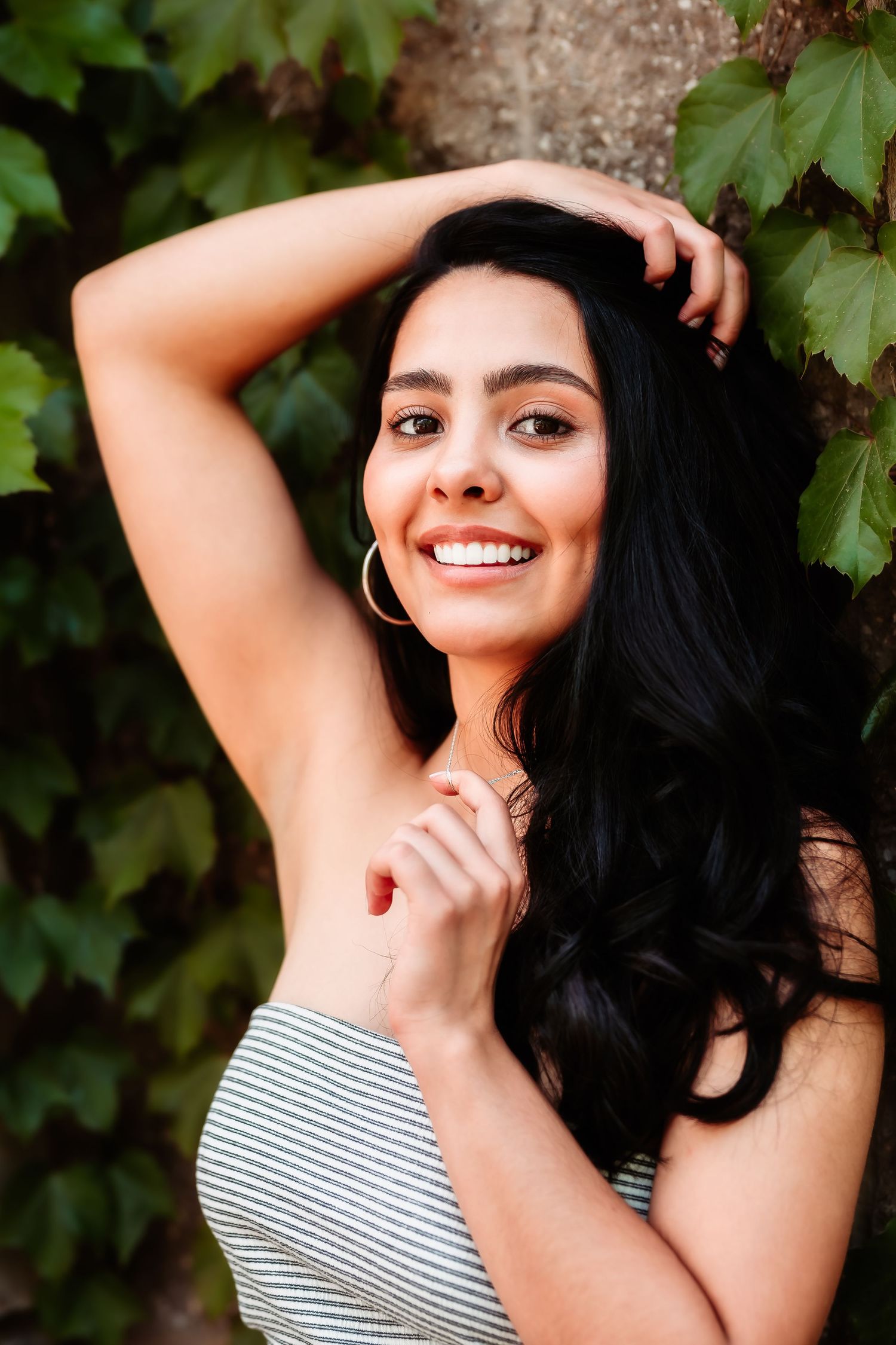 A closeup portrait showing someone in a striped top with flowing dark hair against green leaves.
