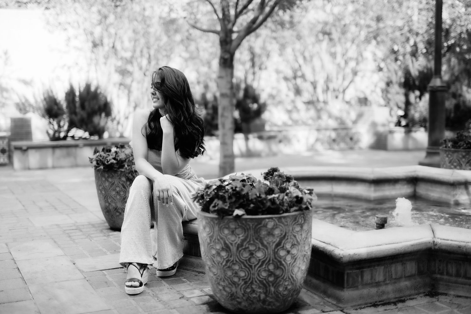 Black and white photo of someone sitting thoughtfully by decorative garden planters.