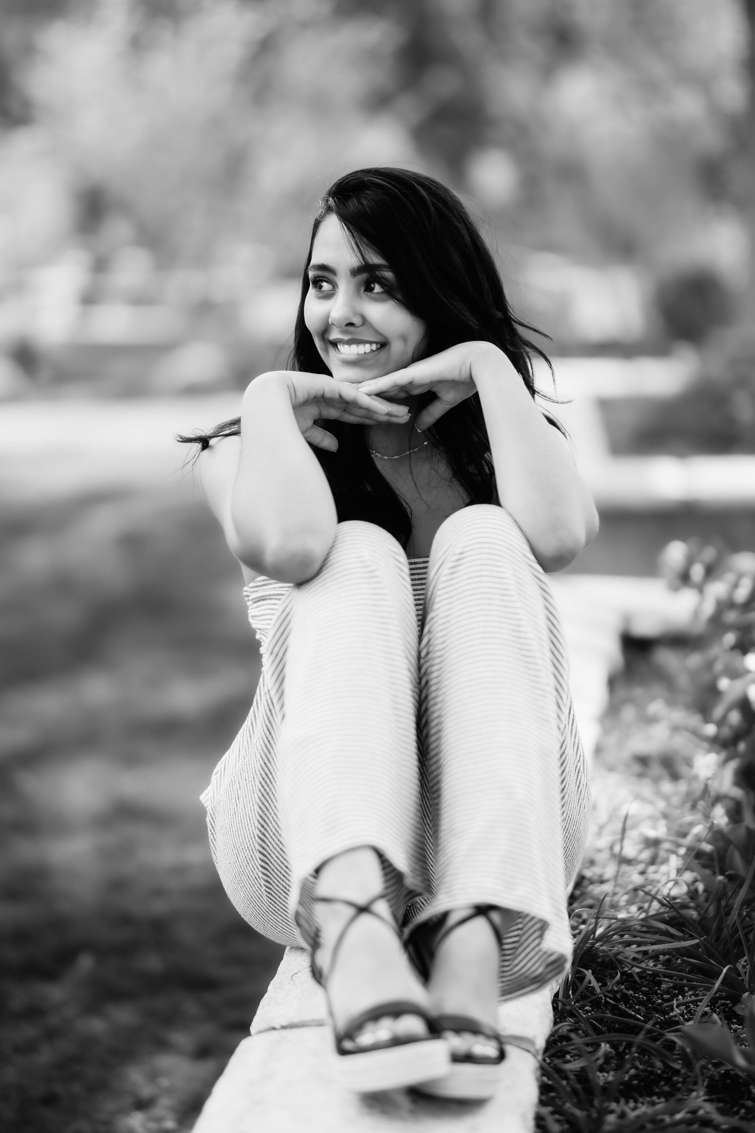 Black and white portrait of person in light clothing resting chin on hands outdoors.