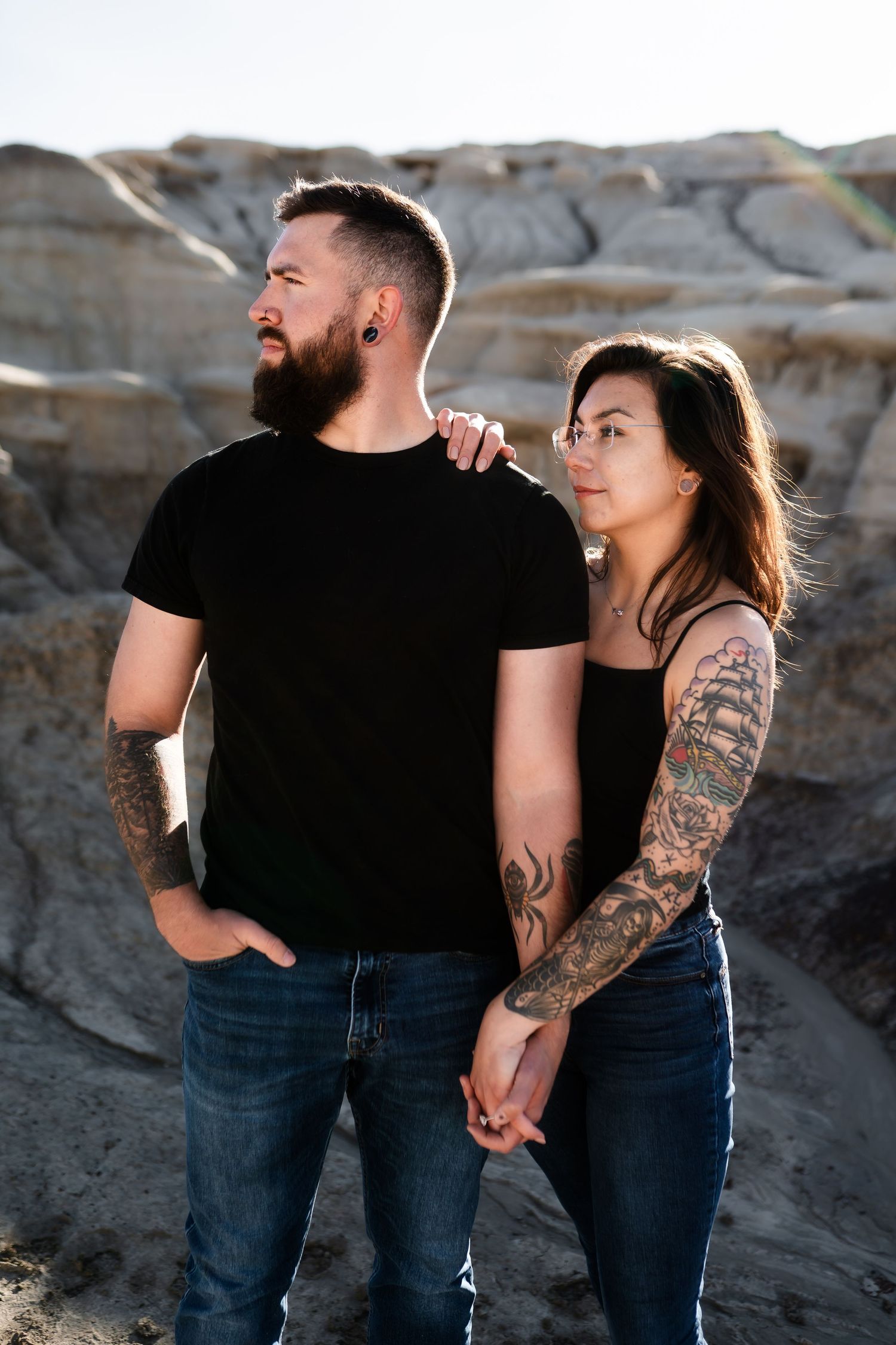 Tattooed couple in casual wear posing against weathered rock formations.