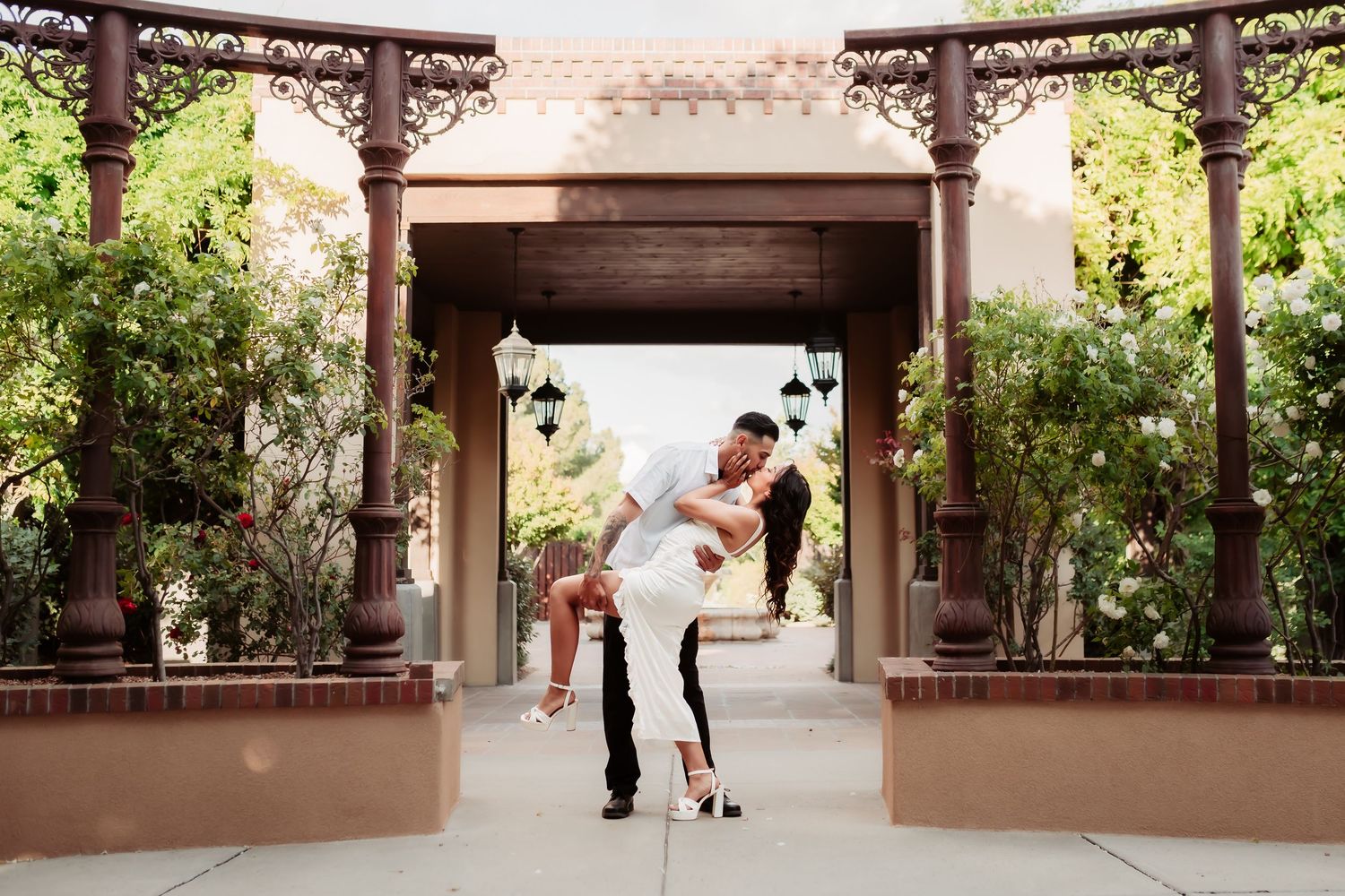 A romantic dip pose under an ornate archway surrounded by greenery and architecture.