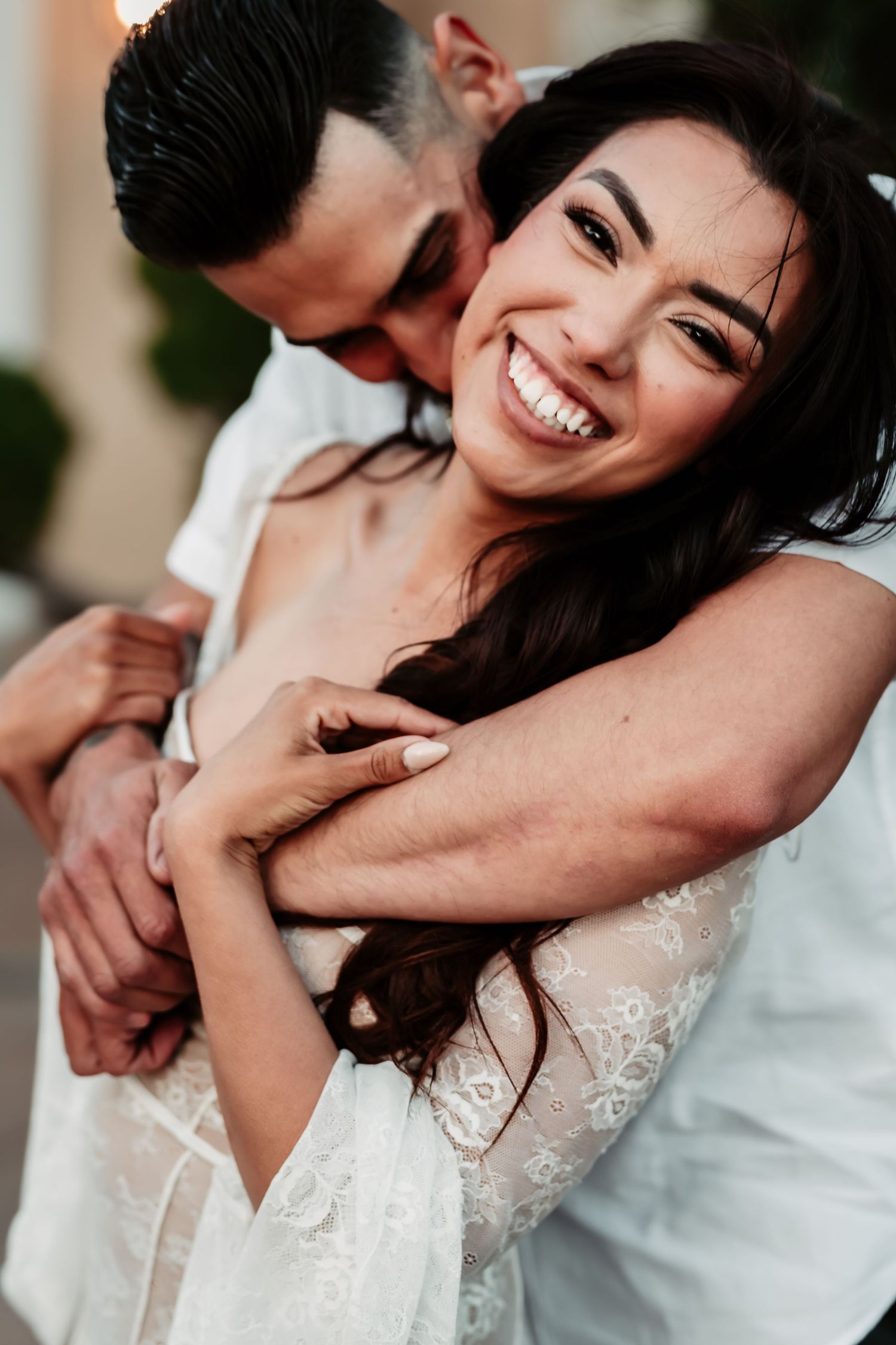 Intimate candid portrait of a couple embracing and laughing while wearing white formal attire.