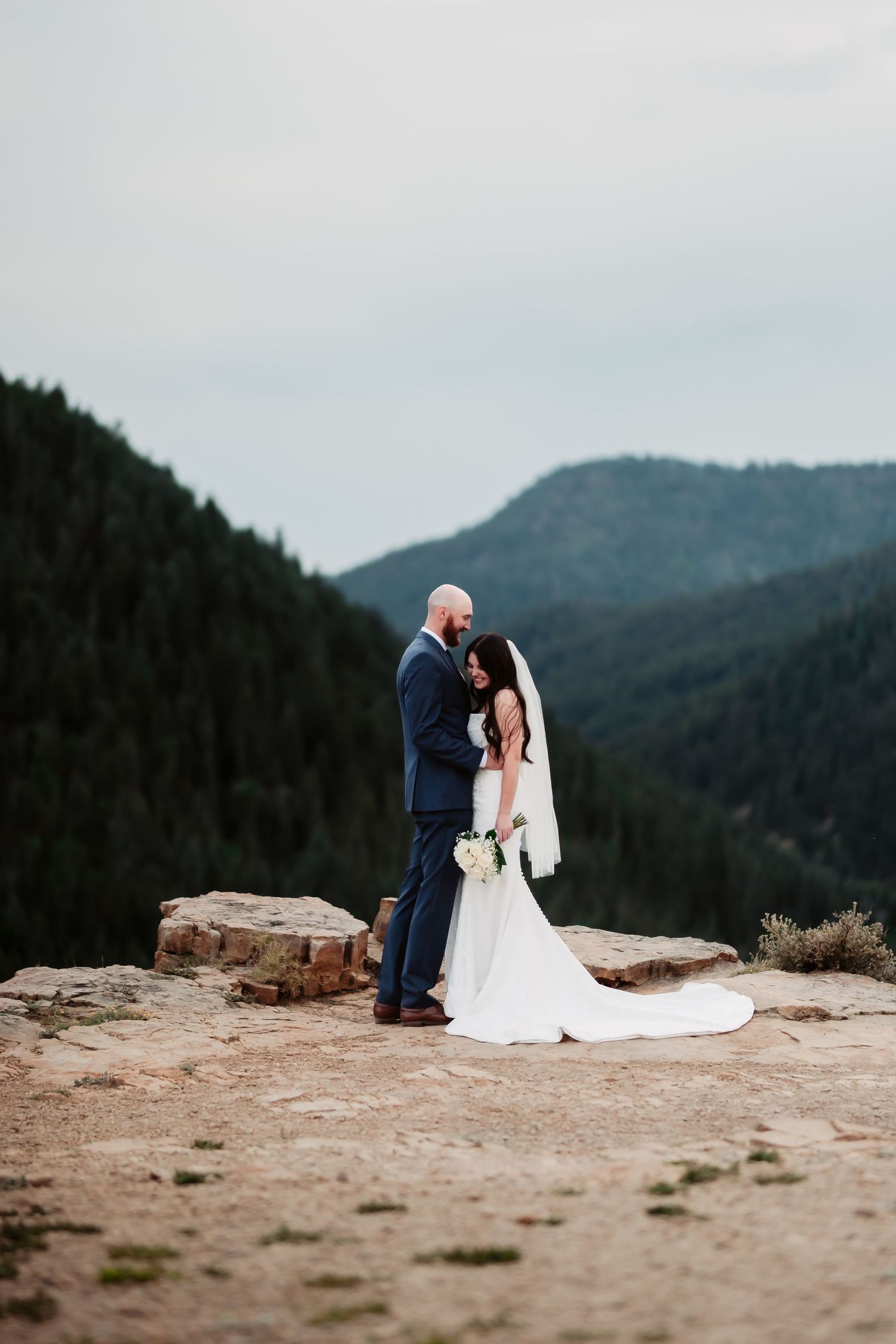 A tender moment between newlyweds on a mountain cliff with dramatic valley views at dusk.