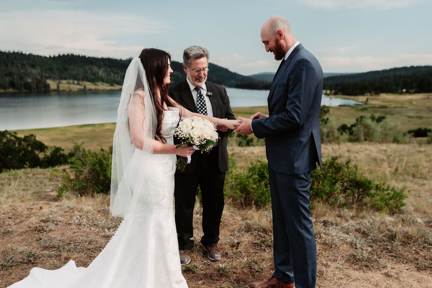 A couple exchanges vows during their outdoor wedding ceremony with a lake in the background.
