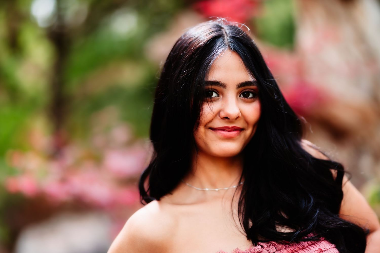 Portrait of someone with flowing dark hair wearing pink against blurred floral background.