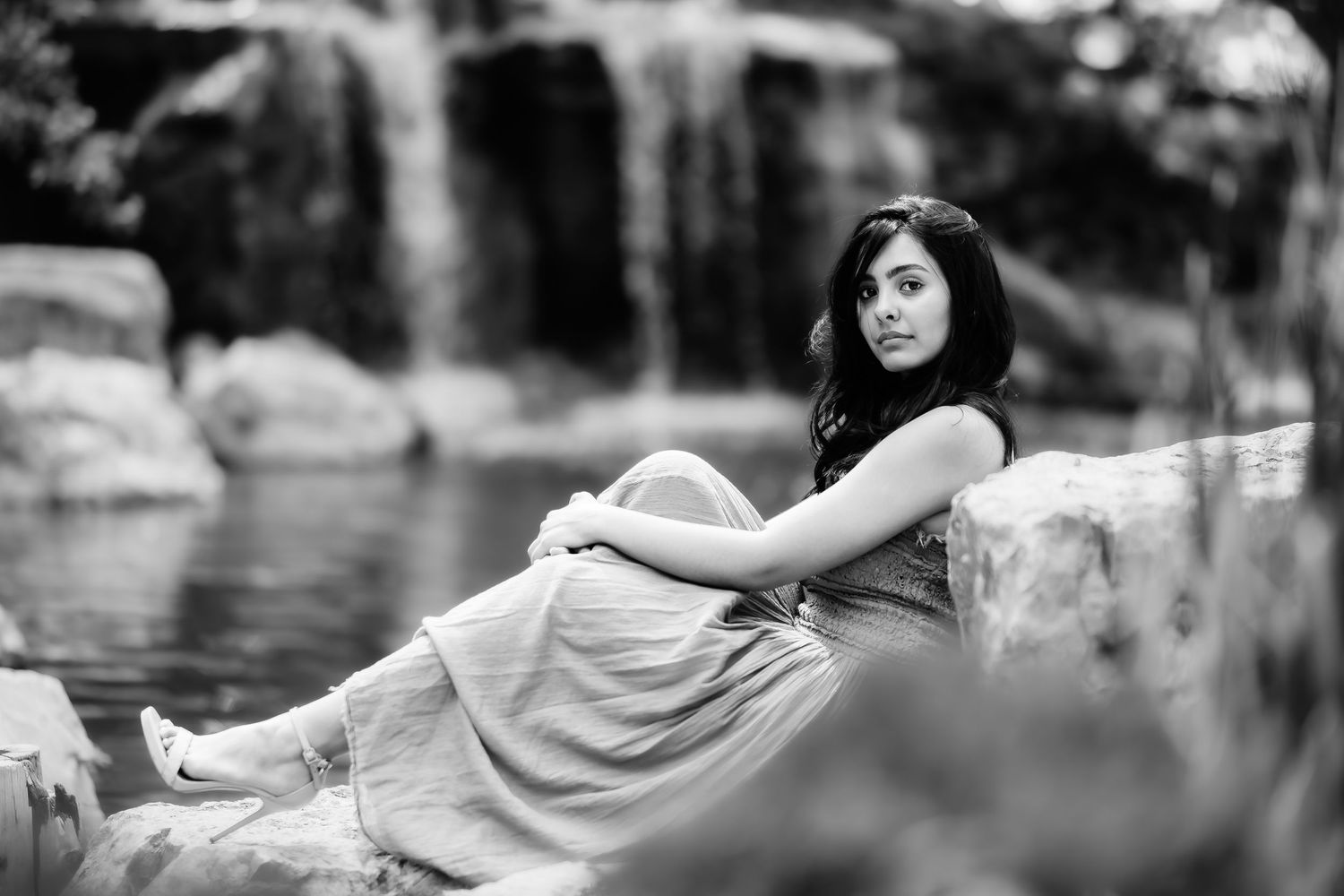 Monochrome image of someone reclining on rocks beside a waterfall.