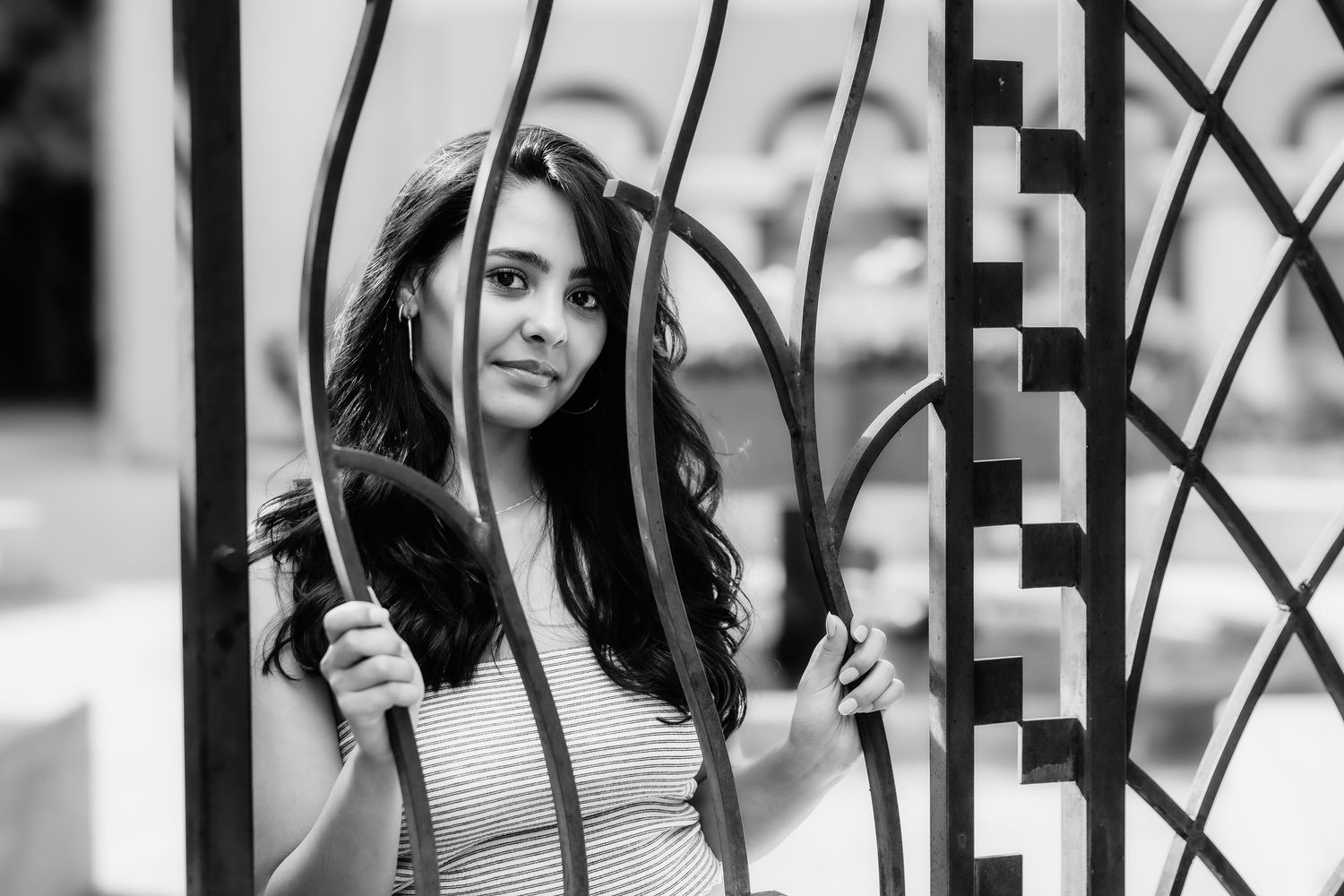 A black and white portrait of a woman posing through decorative iron gates.
