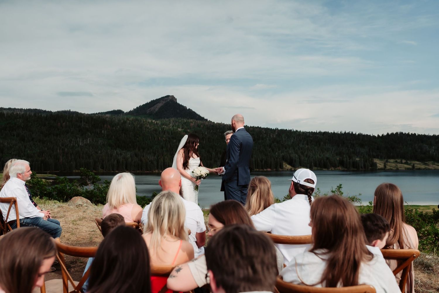 Wedding ceremony overlooking mountain lake with wooden chairs and scenic view.