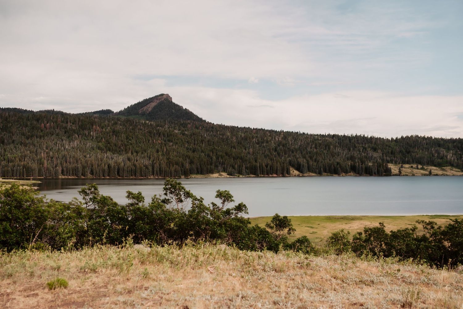 A scenic mountain lake surrounded by pine forest under cloudy skies in a natural landscape.