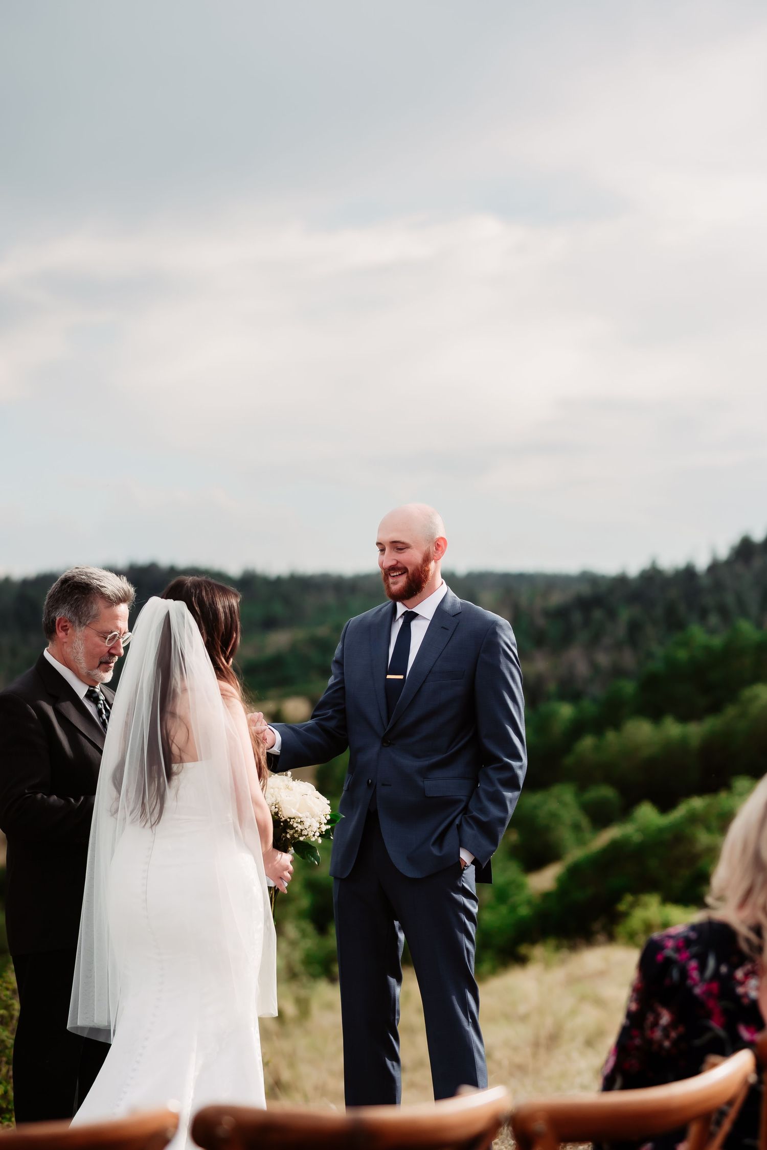 Wedding ceremony taking place on scenic hillside with mountains in background.