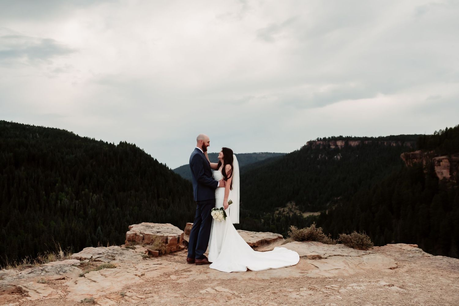 Wedding couple silhouetted against dramatic mountain landscape.
