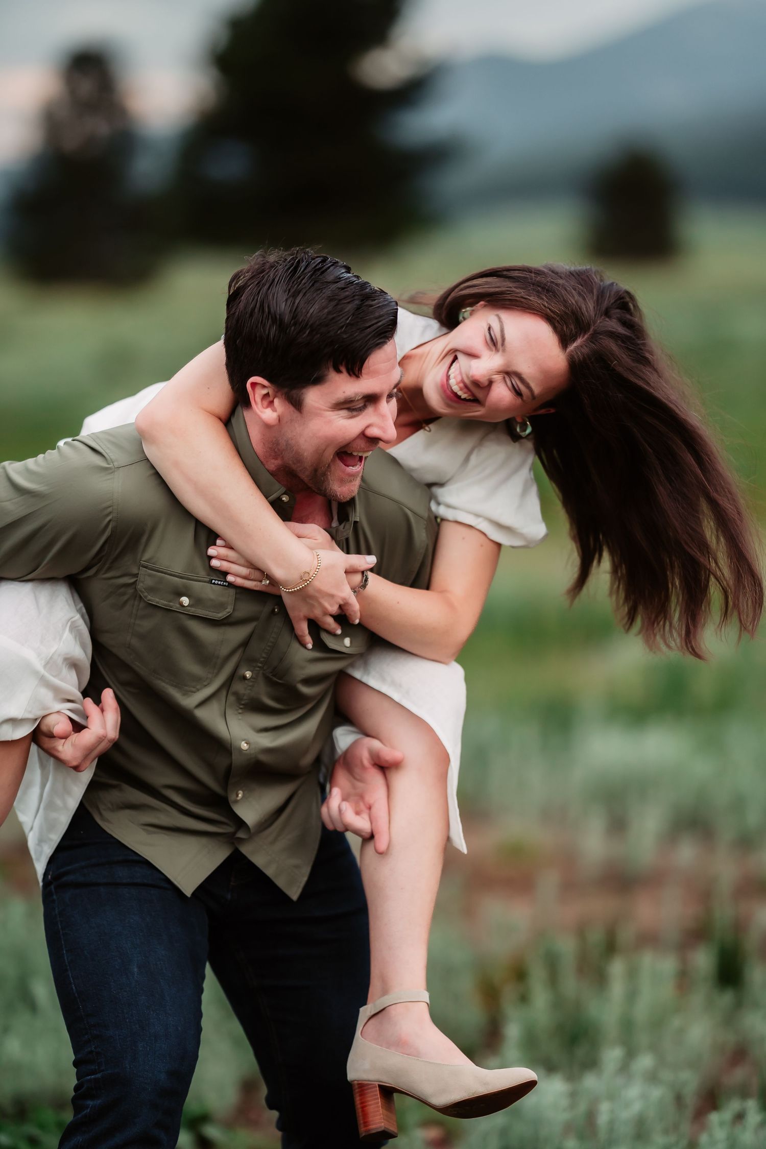 A joyful couple laughs together in a natural outdoor setting as they embrace playfully in casual attire.