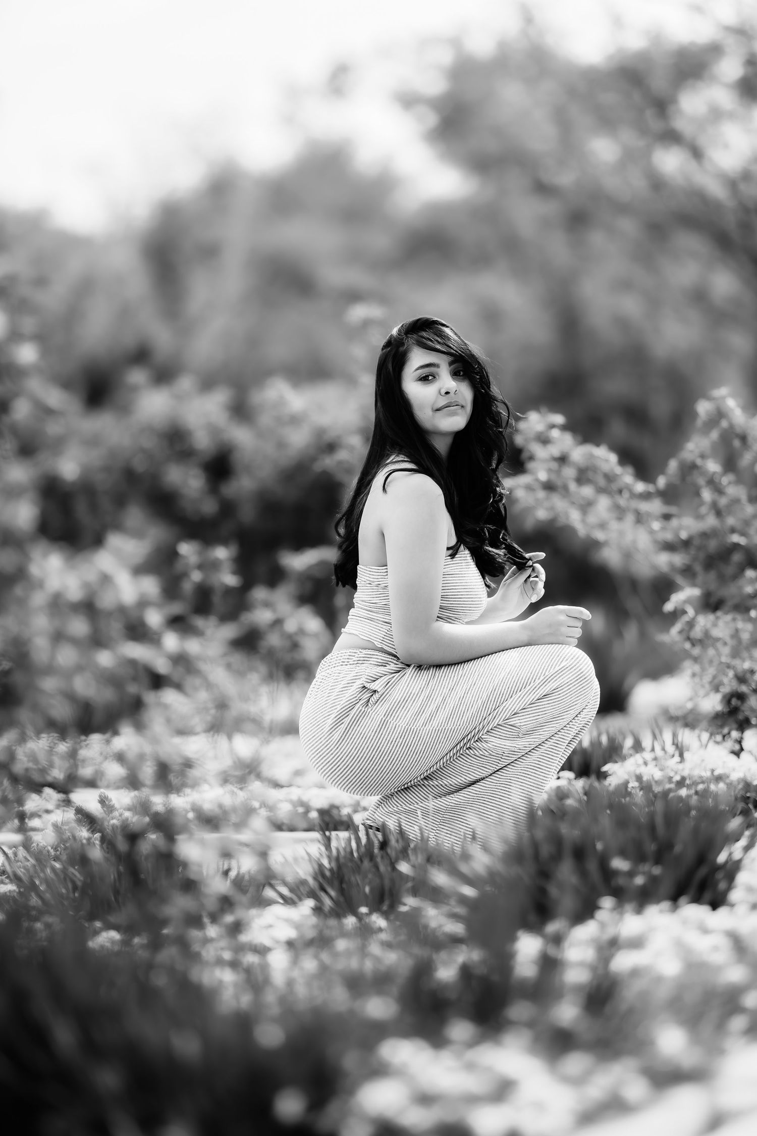 Black and white portrait of person in light-colored outfit crouching in garden setting.