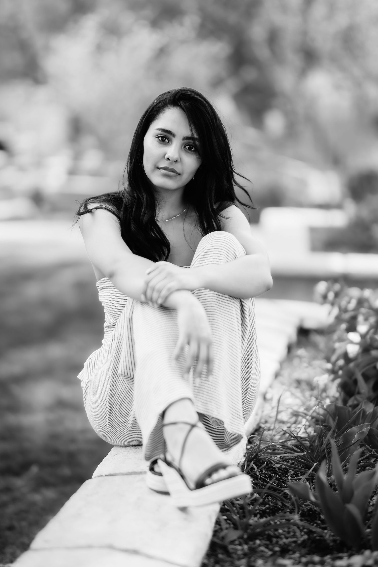 Moody black and white portrait of a person in casual wear sitting on a ledge in nature.