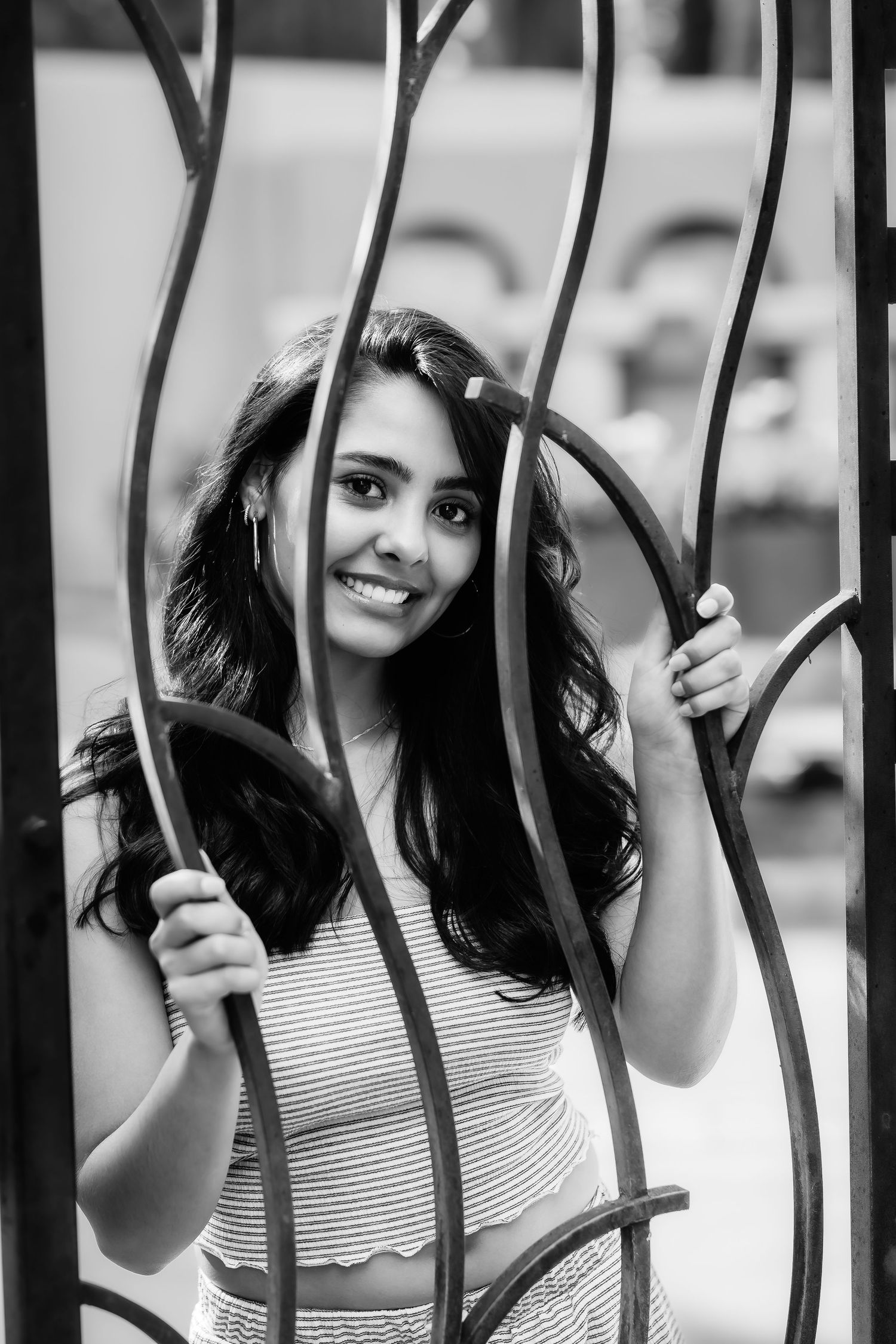 Black and white photo of a figure smiling between decorative metal bars of a gate.