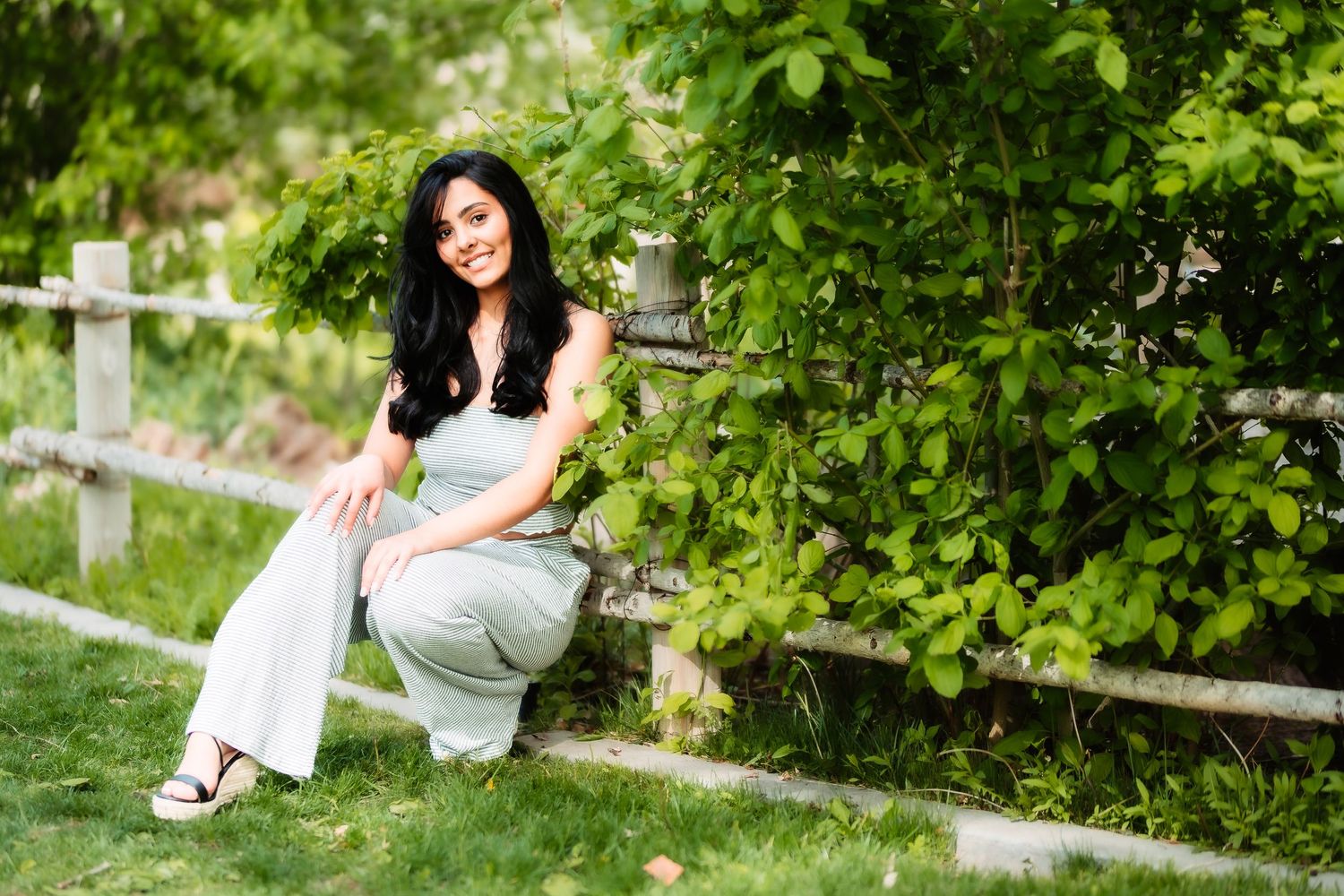 Casual outdoor portrait in white attire against lush green garden background with wooden fence.