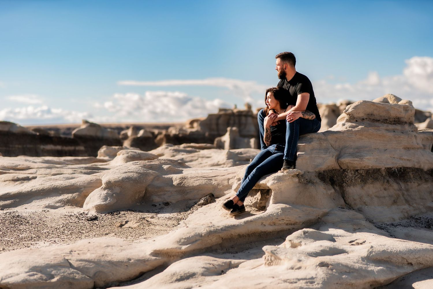 A person sits contemplatively on unique white rock formations against a bright blue sky in a desert landscape.