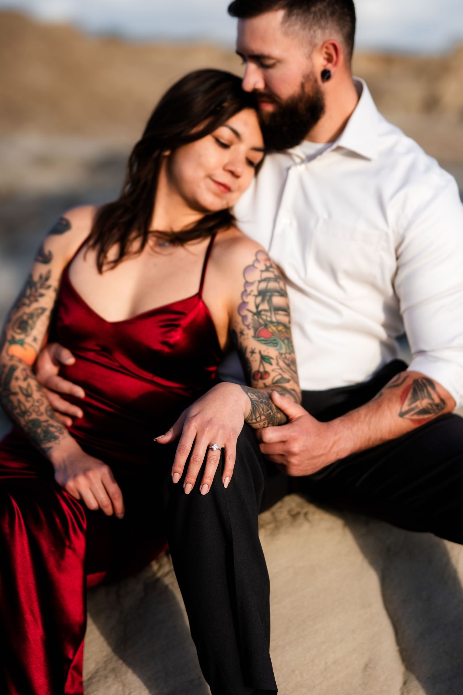 A tattooed couple shares an intimate moment outdoors, with the woman in a red dress and the man in a white shirt.