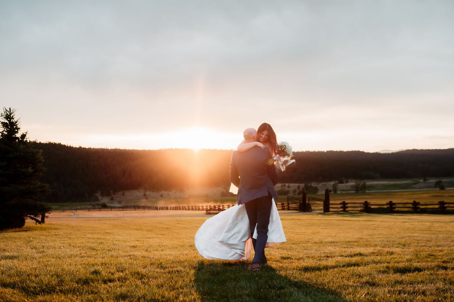 Silhouettes of a couple embracing in a field during a vibrant sunset with mountains in the distance.