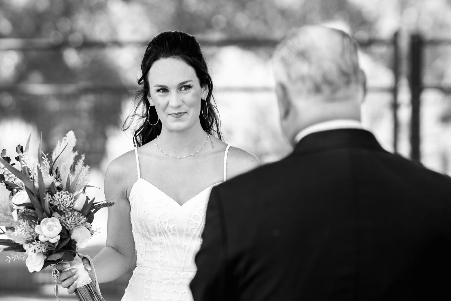 Black and white photo of bride holding bouquet during outdoor wedding ceremony.