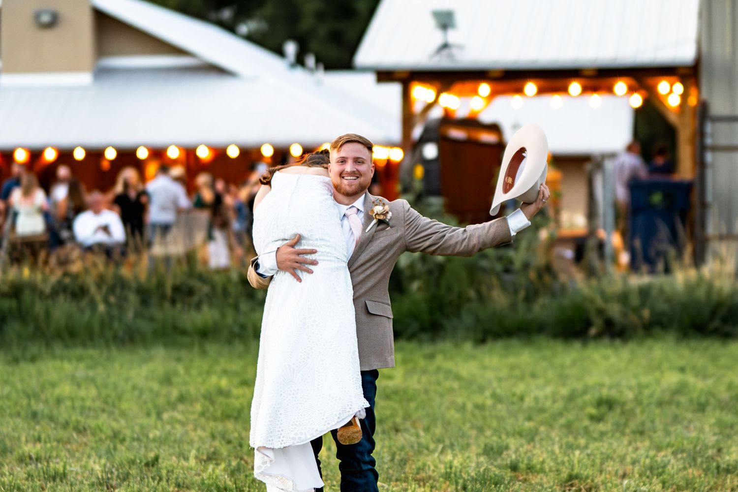 Newlywed couple embracing on the dance floor with string lights in the background.