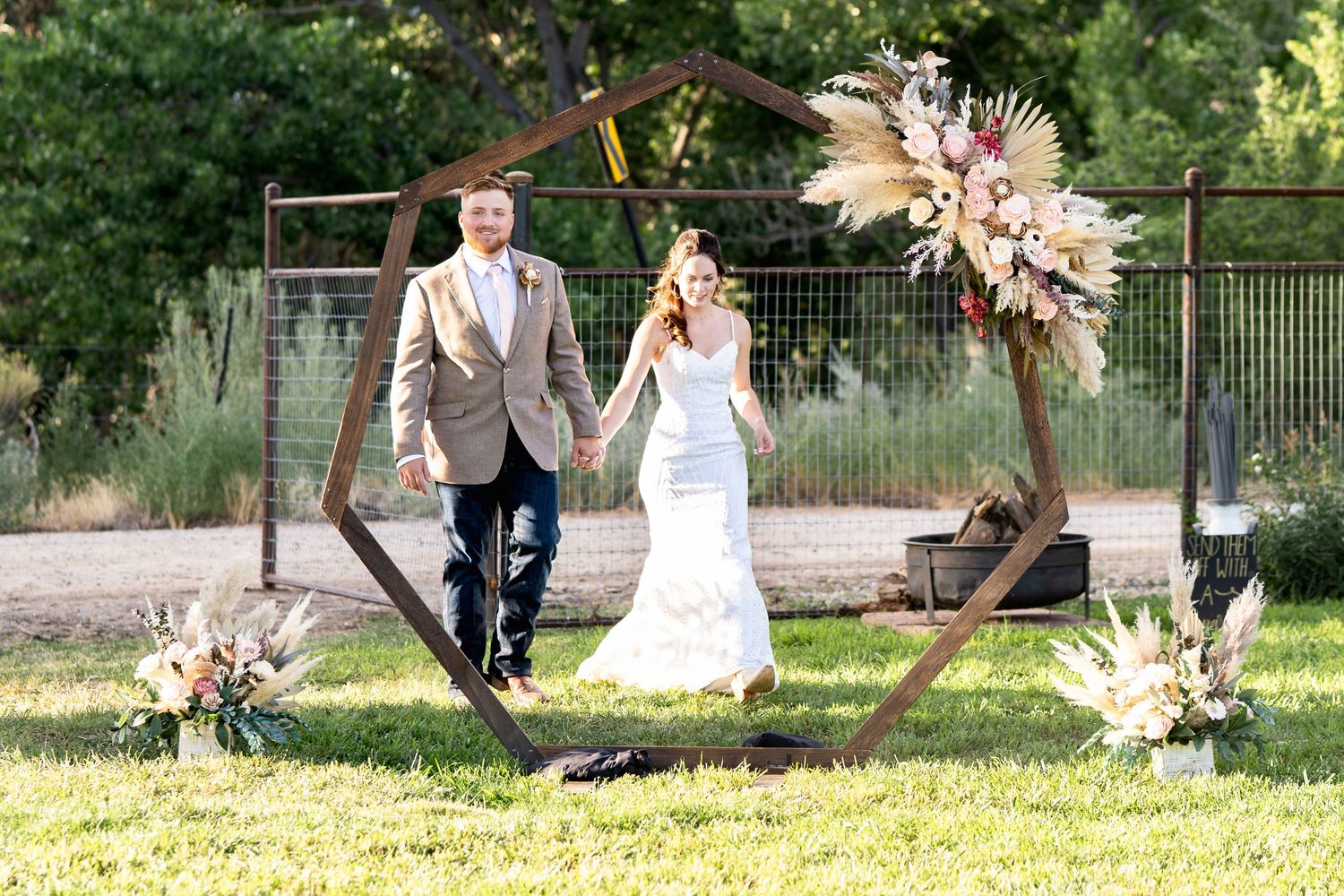 Newlyweds walk together on grass with boho-style floral arrangements and decorative elements.