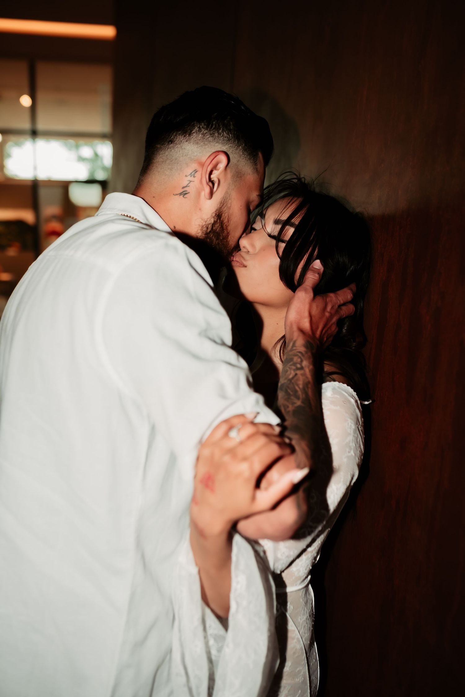 Intimate moment shared between couple in white outfits against dark wall with moody lighting.