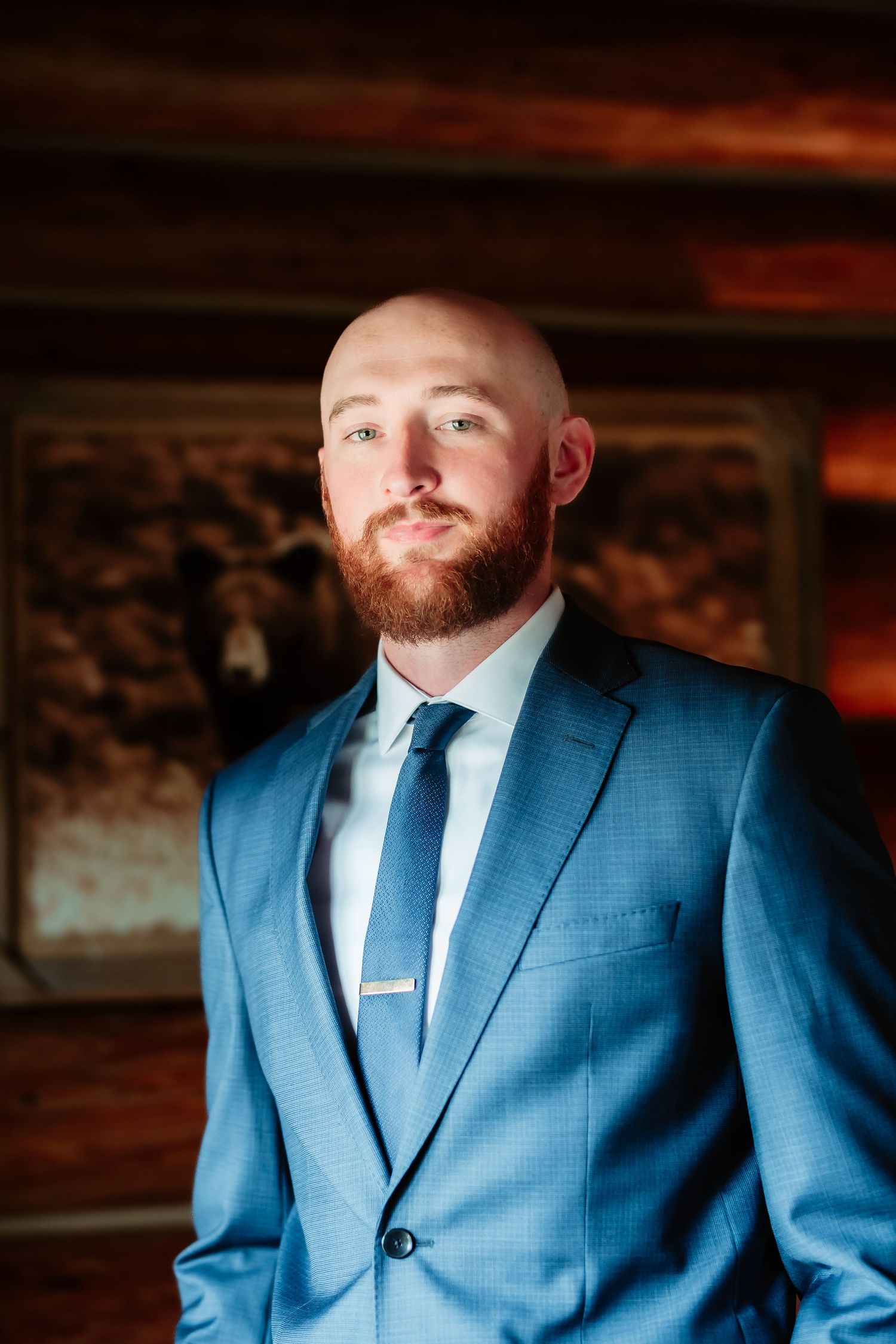 Person in tailored blue suit seated in warm atmospheric lighting against wooden wall interior.