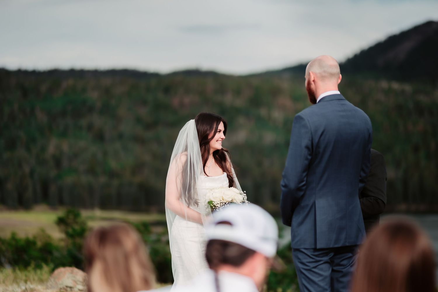 Outdoor mountain wedding ceremony with guests seated on wooden chairs.