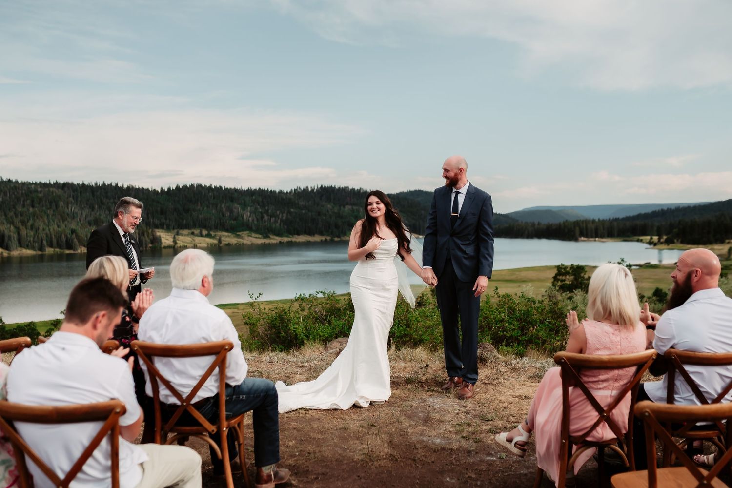 Panoramic view of outdoor wedding ceremony with wooden chairs and mountain backdrop.