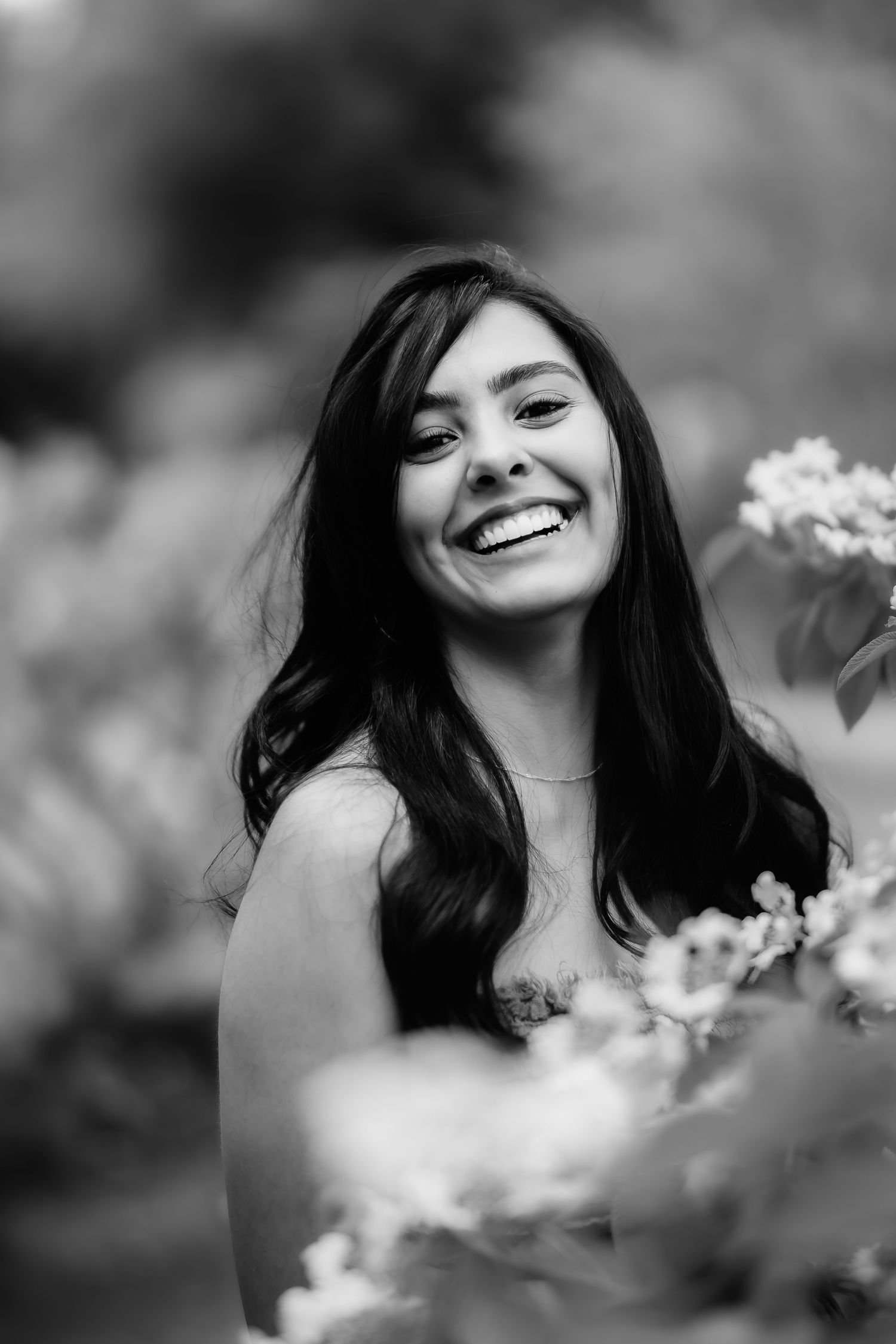 A black and white portrait amidst blooming flowers capturing a joyful expression.
