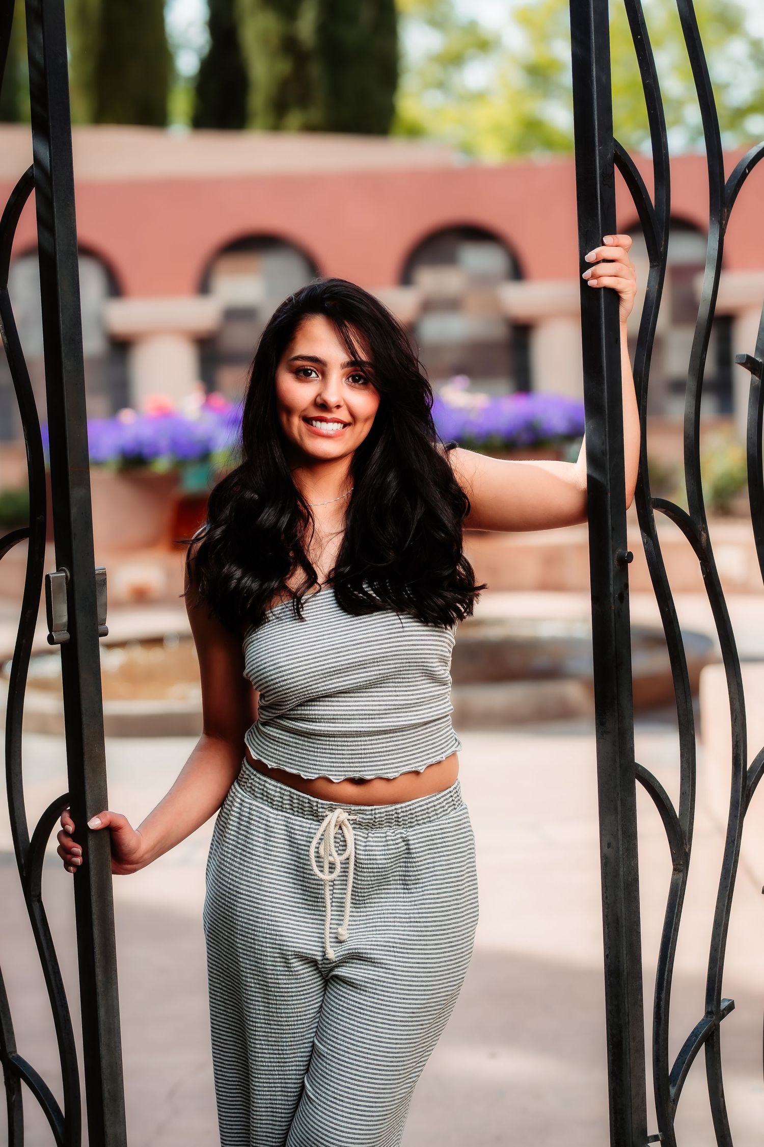 A woman in casual grey attire stands between decorative metal gates with arches in the background.