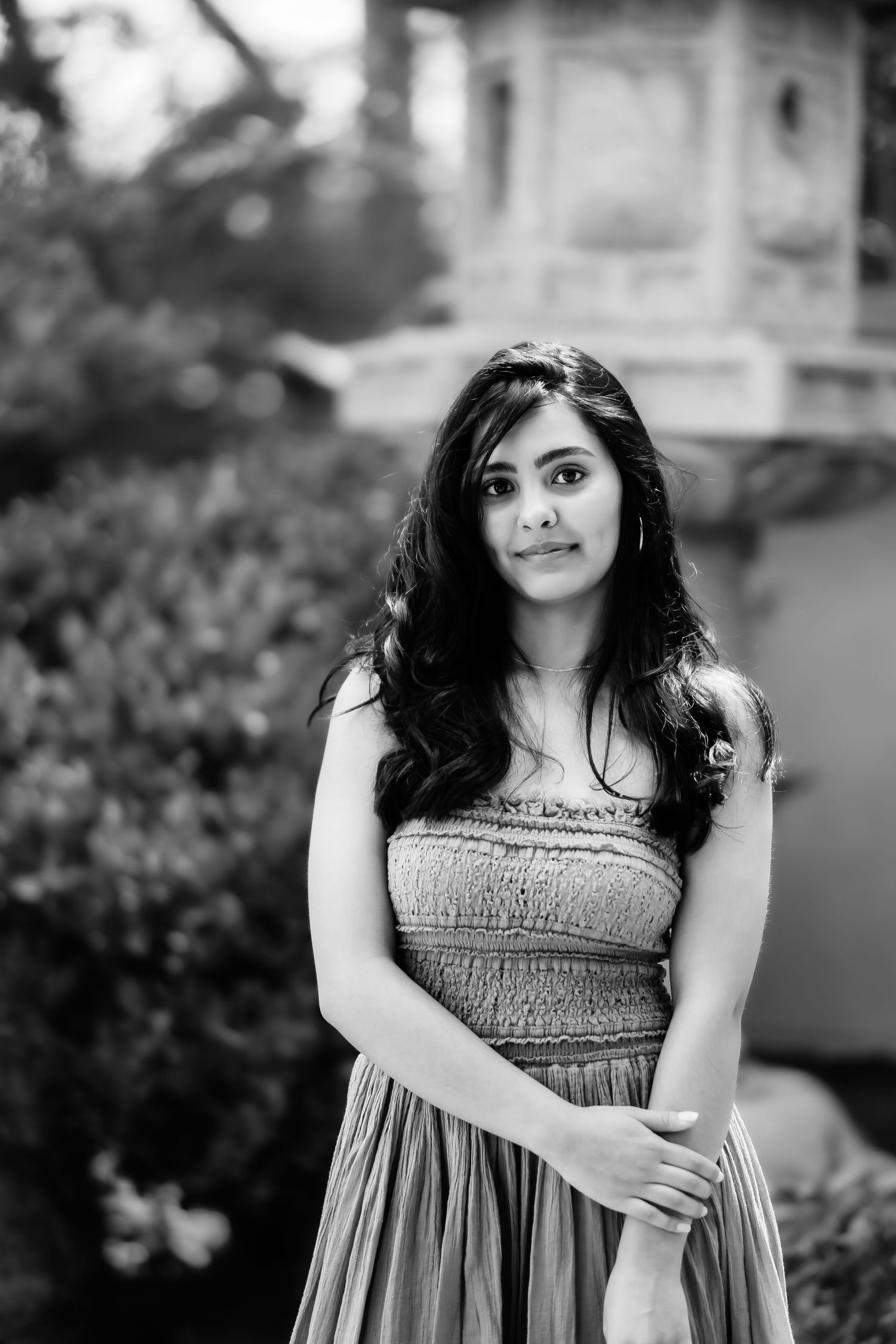 A black and white portrait of someone wearing a textured dress in an outdoor garden setting.